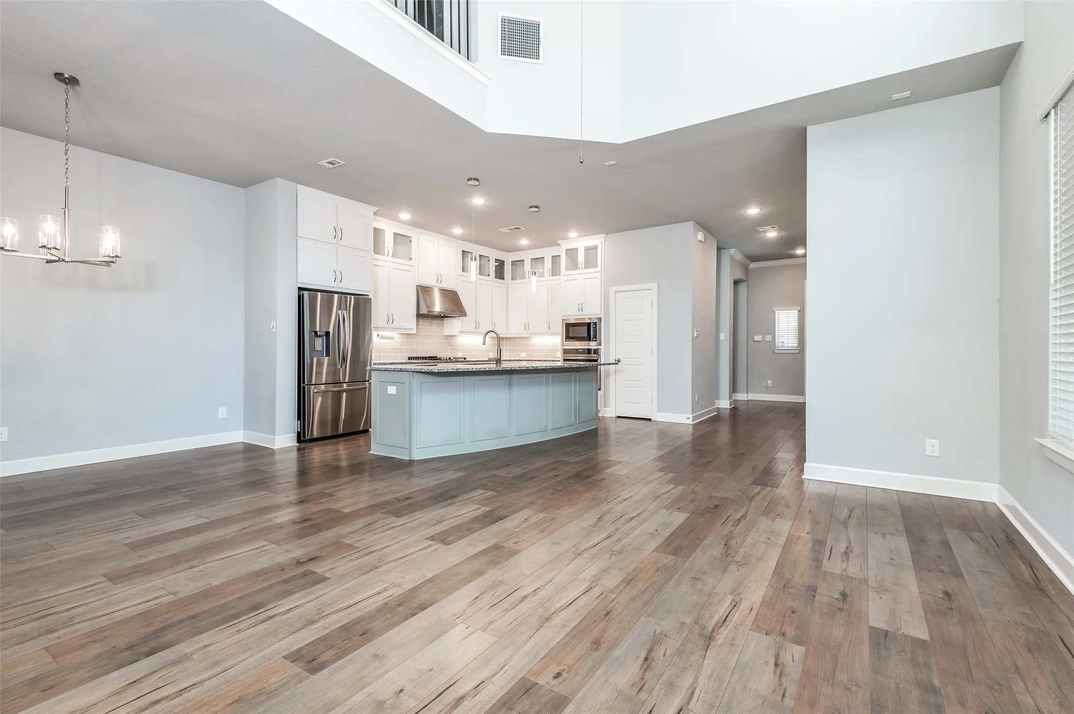 Wood-finish flooring throughout, kitchen with stainless steel appliances, central island with seating, pendant lighting, and recessed lighting
