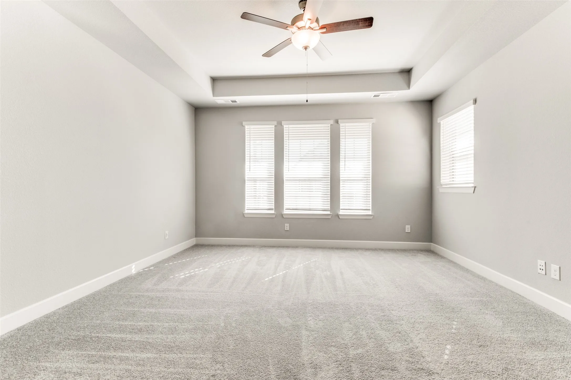 Light gray carpeting, a tray ceiling, and a ceiling fan with light fixture