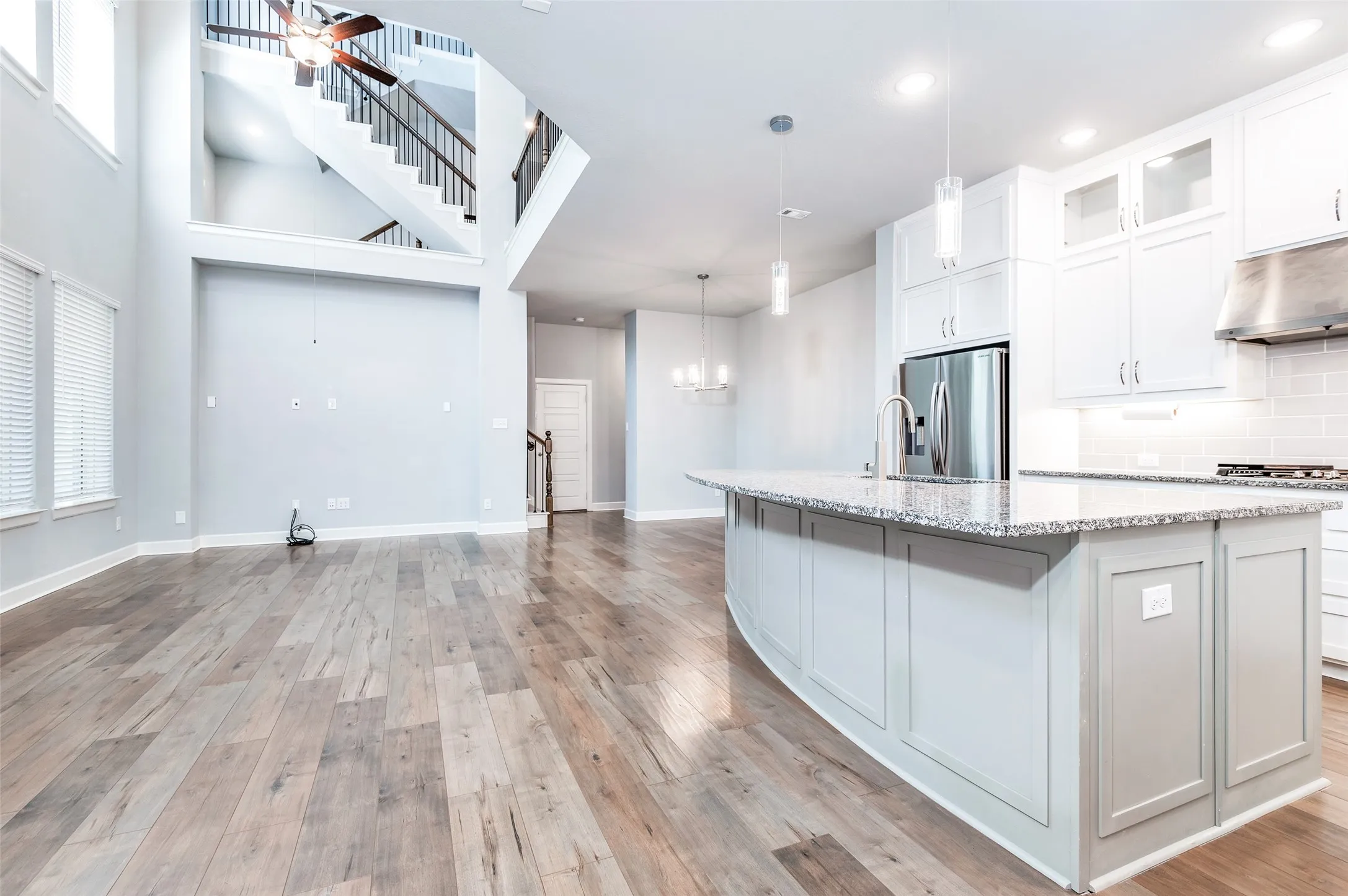 Open-concept living area featuring wood-finish flooring, a two-story ceiling, and a modern kitchen with a large island and stainless steel appliances