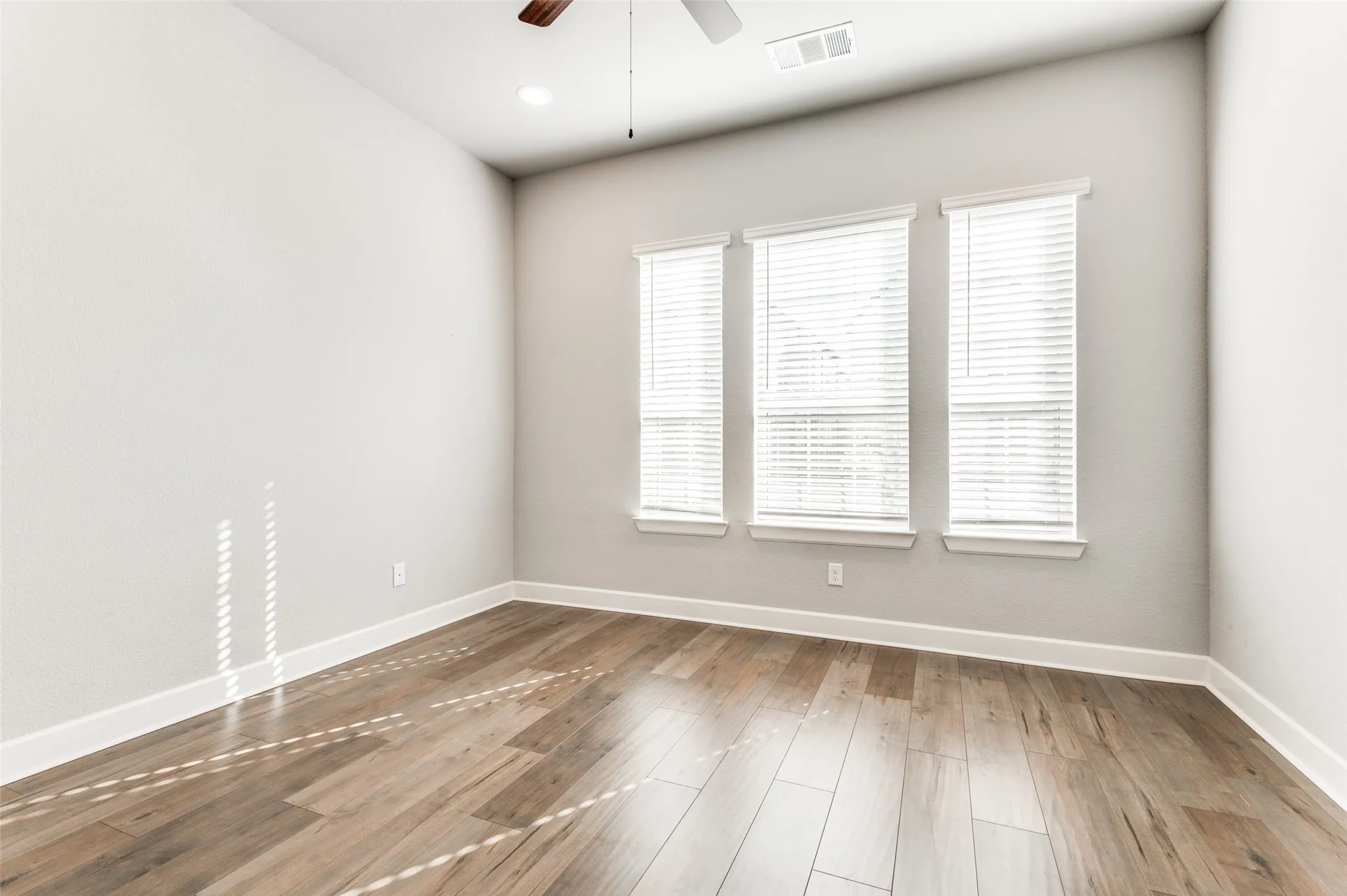 Wood-finish flooring, three windows with blinds, recessed ceiling light, ceiling fan, and white trim