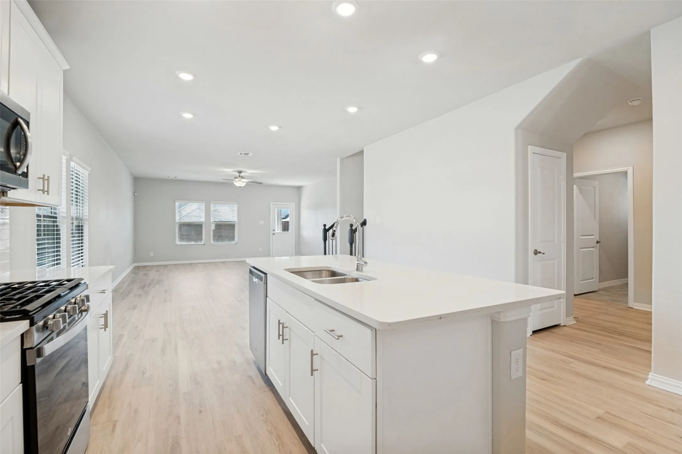 Kitchen island with a double basin sink, white cabinetry, integrated dishwasher, and light-toned wood-finish flooring throughout