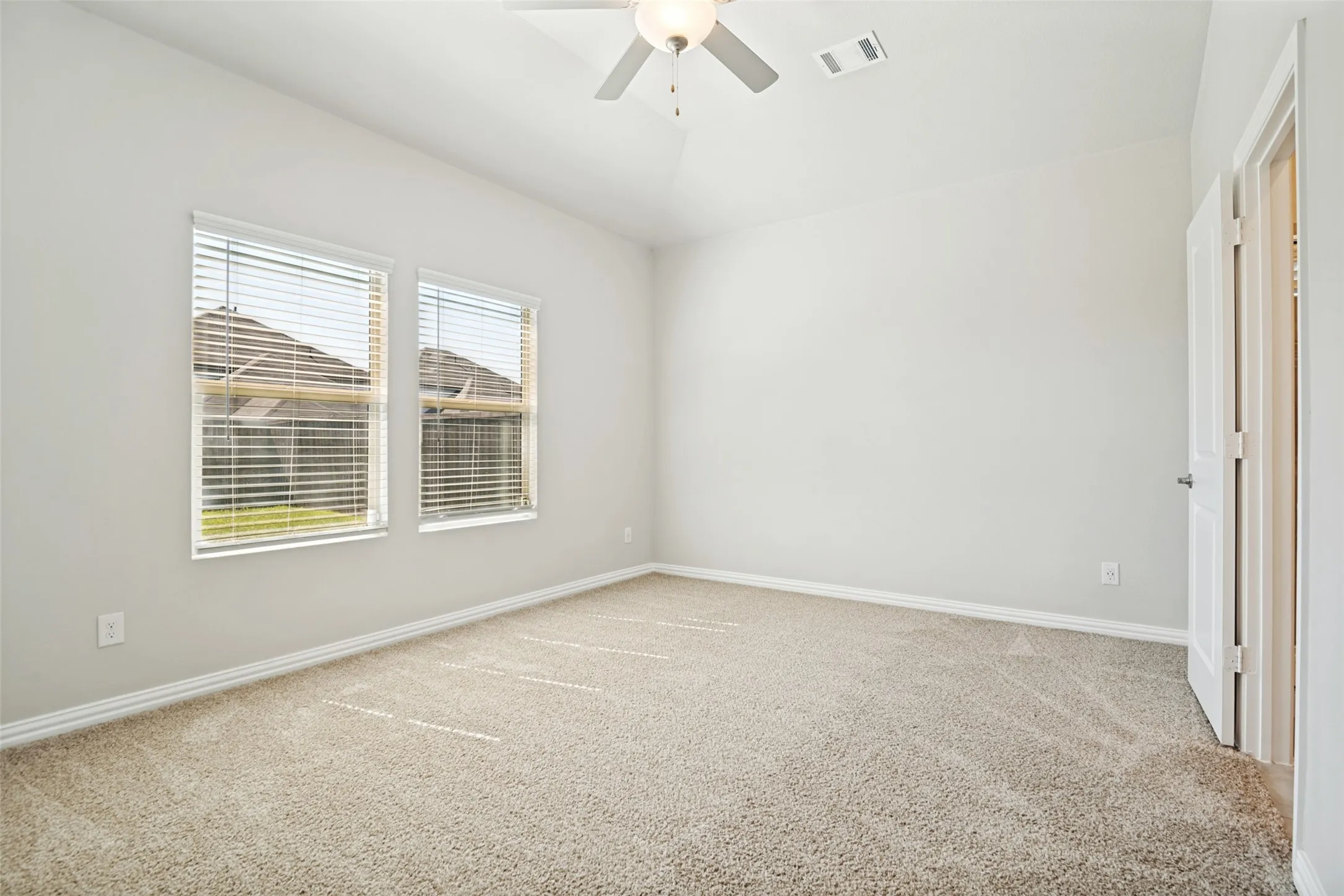 Two windows with blinds, neutral carpet, ceiling fan with light, and white paneled door