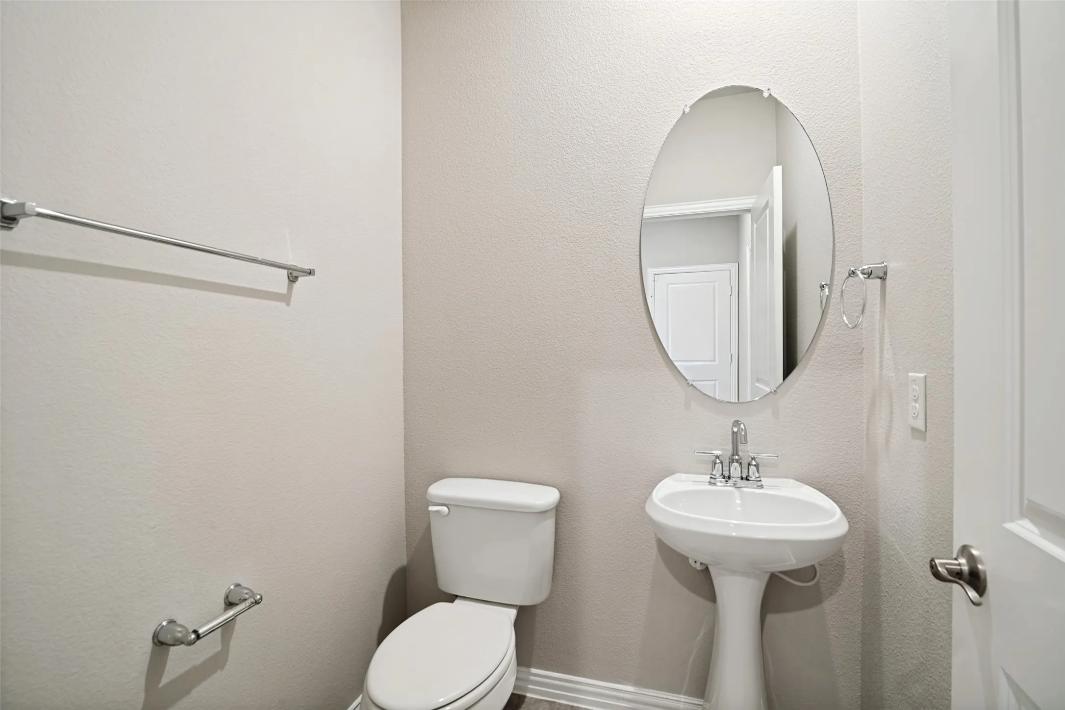 Pedestal sink with chrome faucet, oval mirror, and white toilet