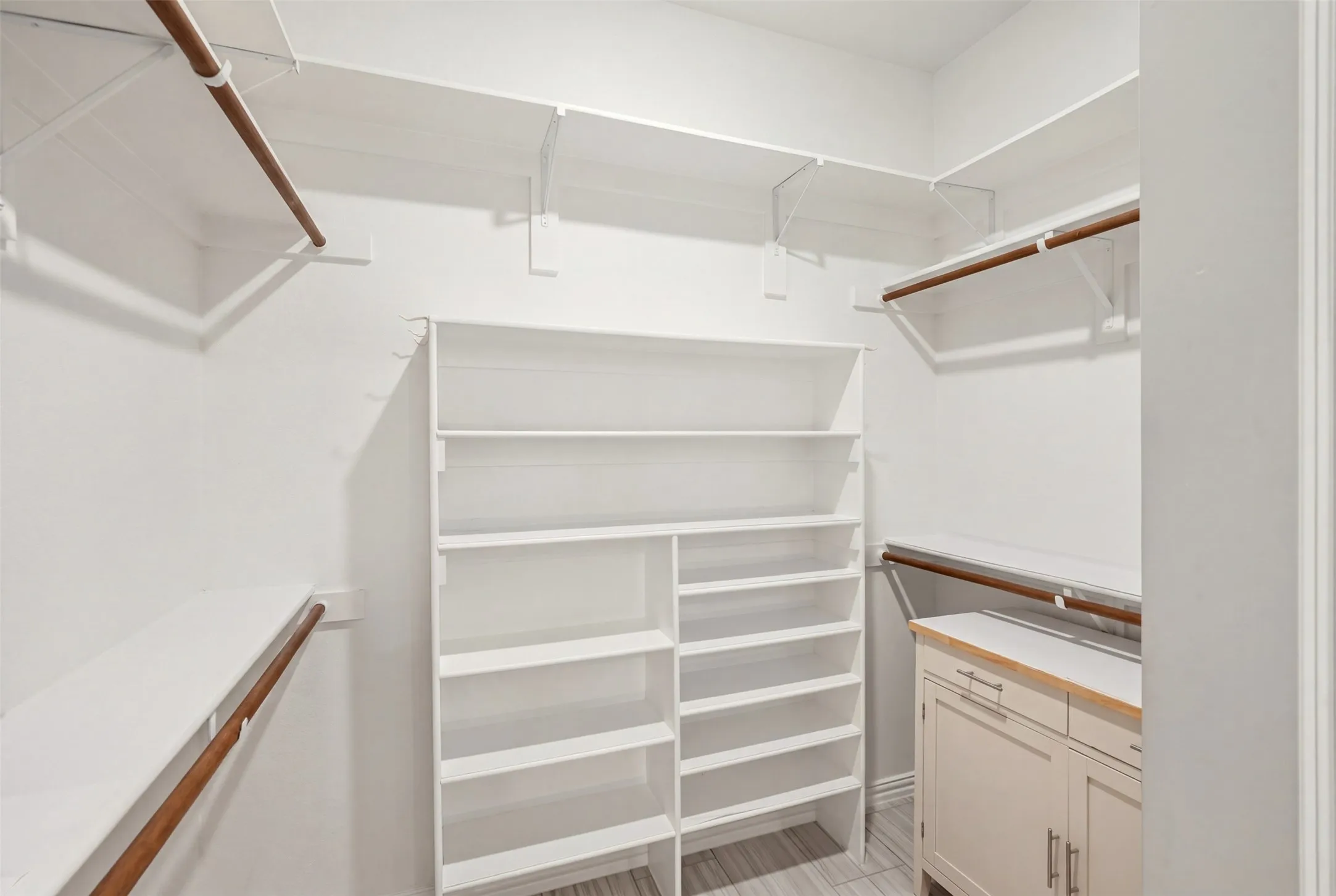 Built-in closet system with multiple shelving units, hanging rods, and a lower cabinet with a wood-finish countertop