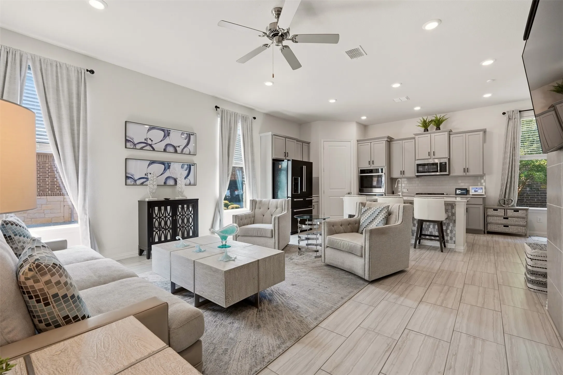Open-concept living space with light-tone tile flooring, recessed lighting, ceiling fan, and kitchen featuring light gray cabinetry and stainless steel appliances