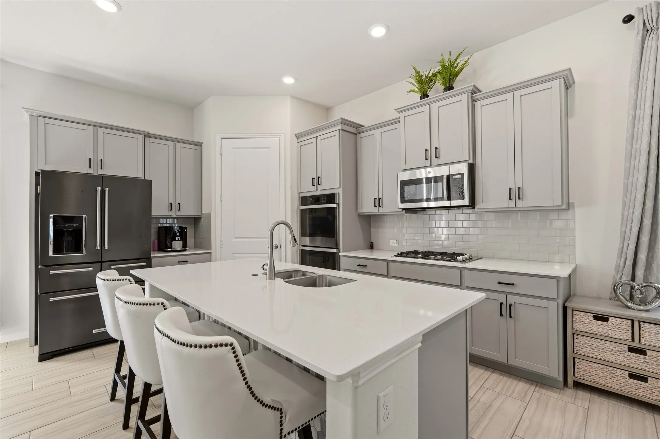 Kitchen featuring gray shaker cabinetry, stainless steel appliances, a center island with an integrated sink, white subway tile backsplash, and wood-finish flooring