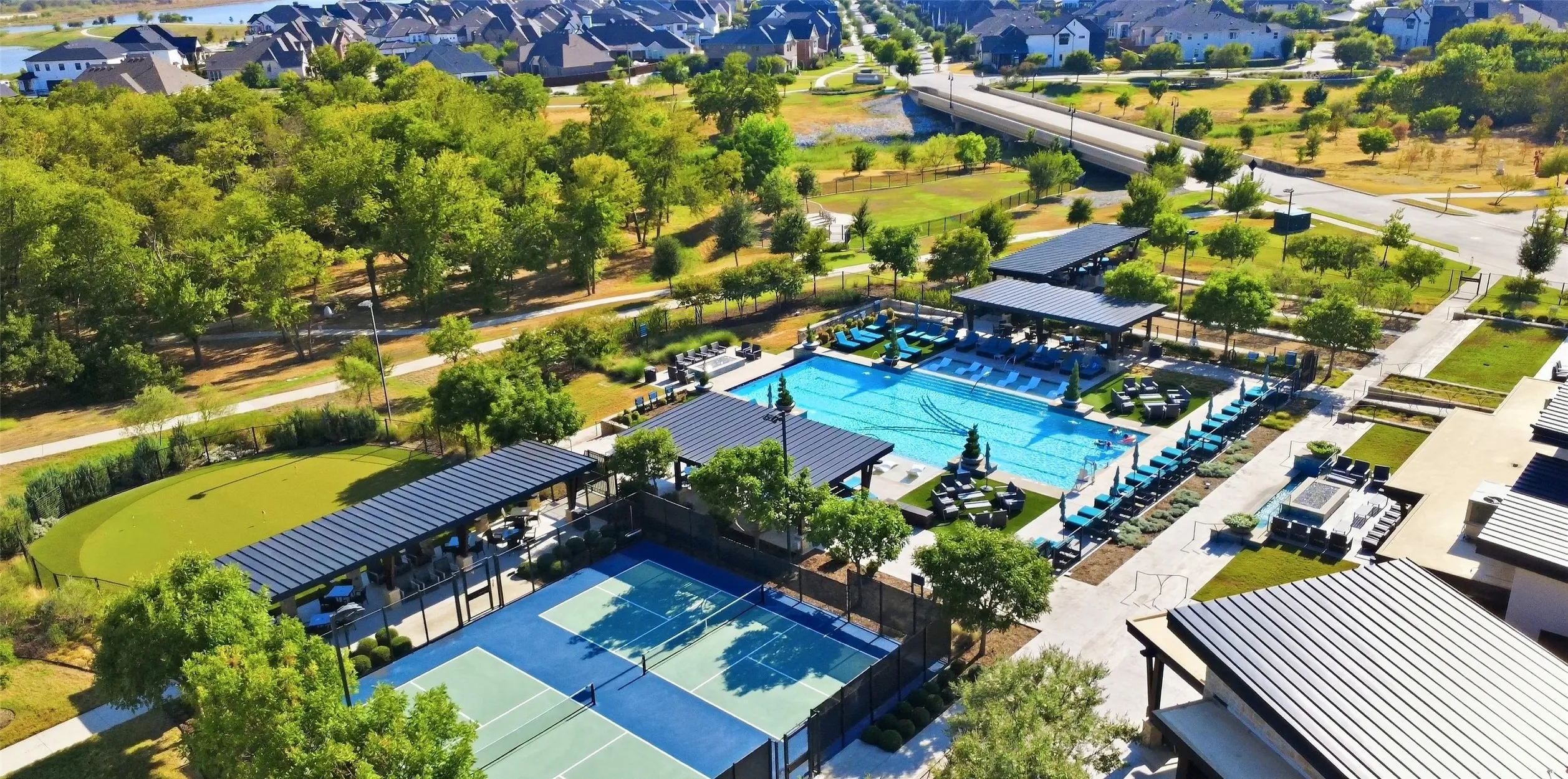 Expansive outdoor recreation area featuring a large swimming pool, two tennis courts, a putting green, and covered lounge spaces