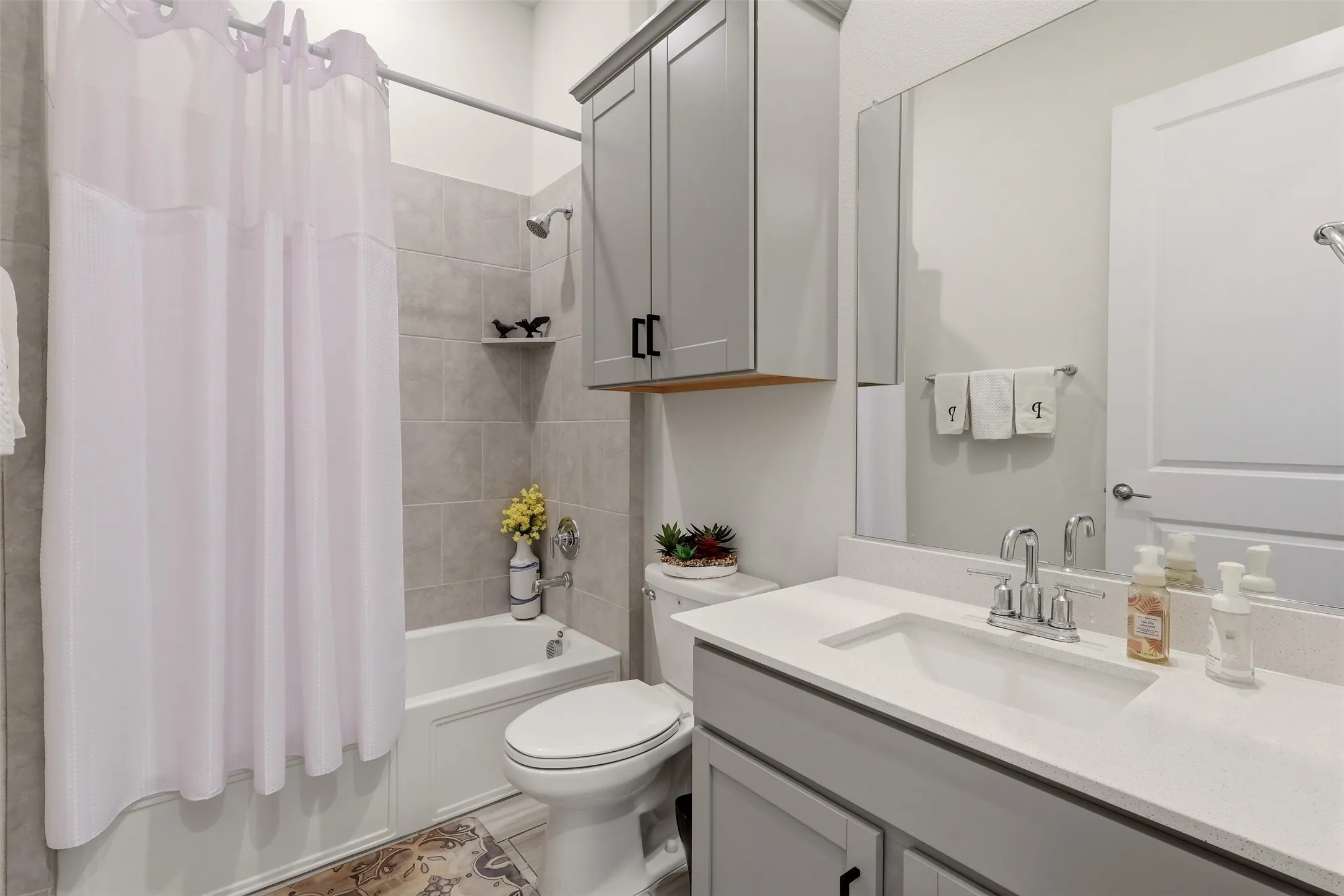 Full bathroom featuring a tub/shower combination with light gray tile surround, single vanity with integrated sink, and gray cabinetry