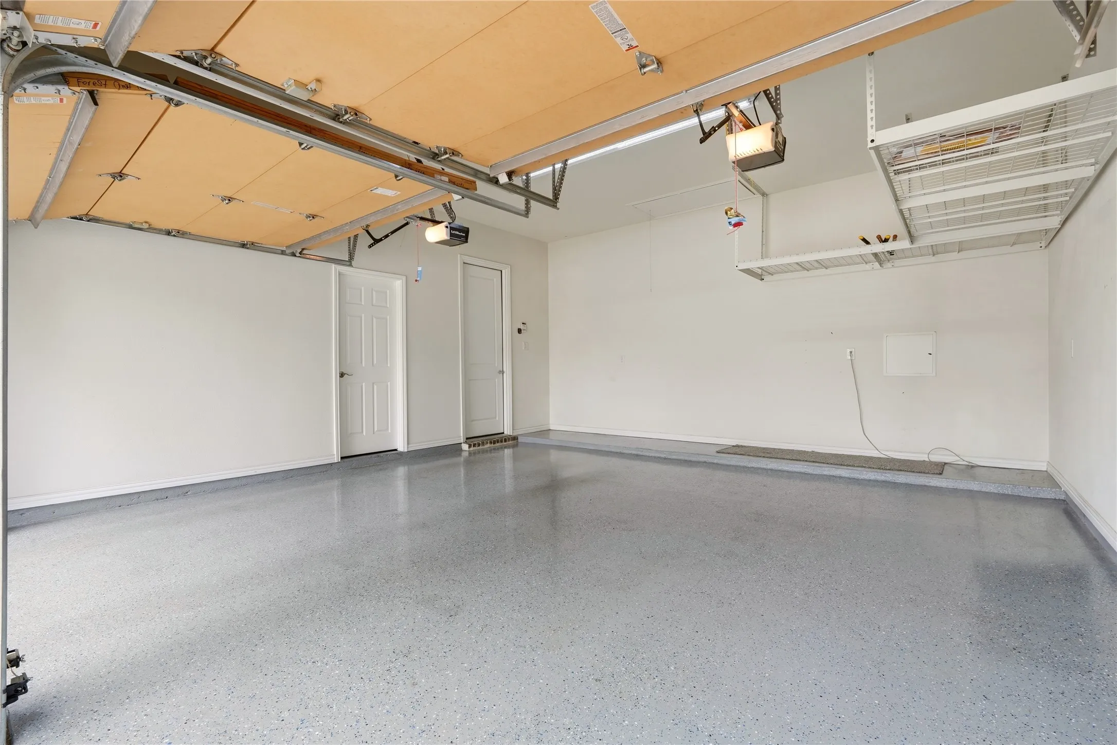 Spacious garage with light grey speckled flooring, white walls, and built-in overhead storage racks