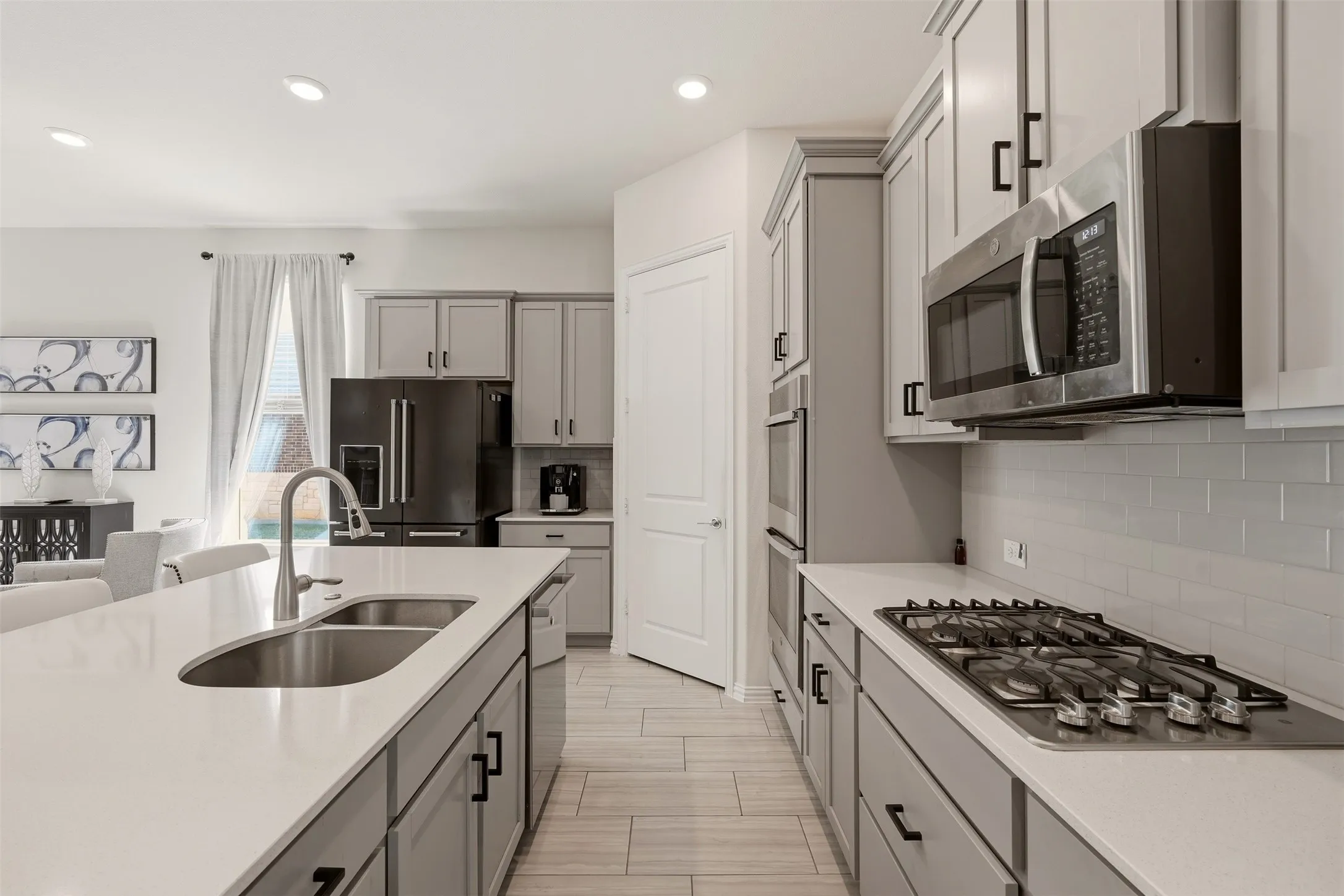 Kitchen featuring light gray cabinetry, stainless steel appliances, a gas cooktop, a built-in microwave, and an island with an undermount sink
