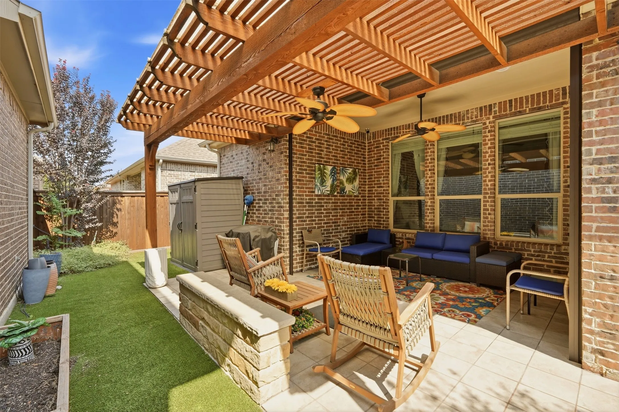 Covered patio with a wood-tone pergola, brick exterior, ceiling fans, and tiled flooring