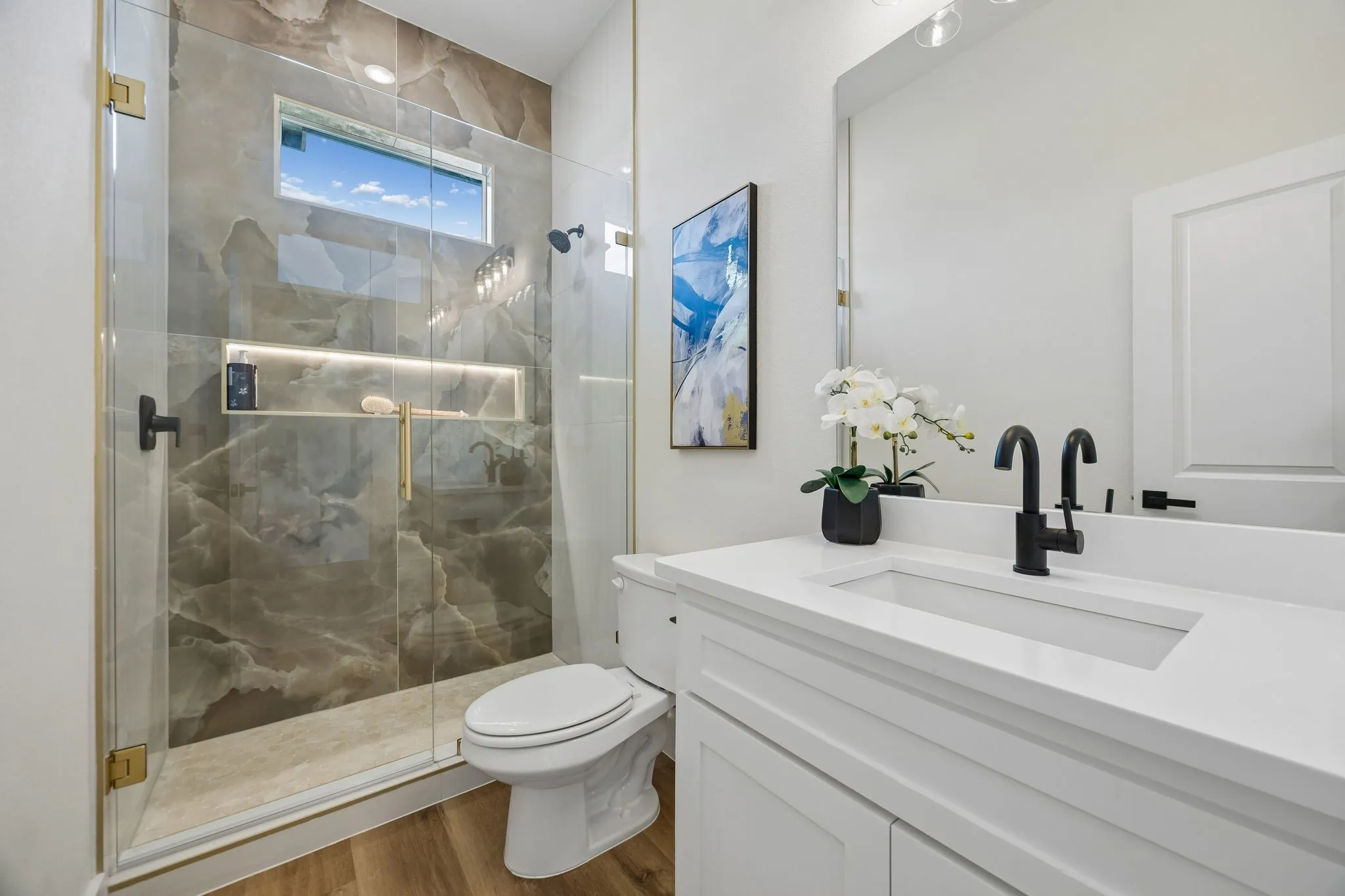 Glass-enclosed shower with stone-finish wall tile, a built-in recessed shelf with integrated lighting, and a transom window