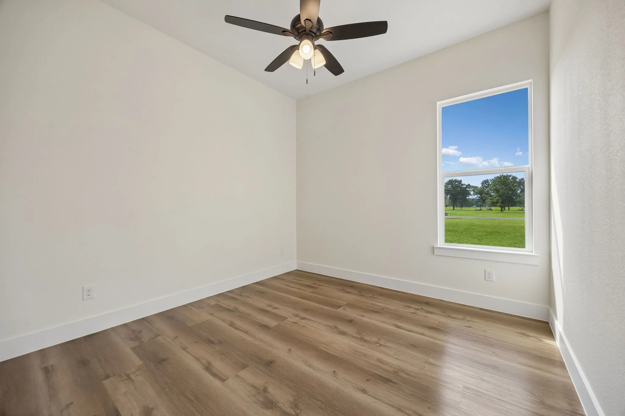 Neutral wall color, wood-finish flooring, ceiling fan with integrated lighting, and a large window