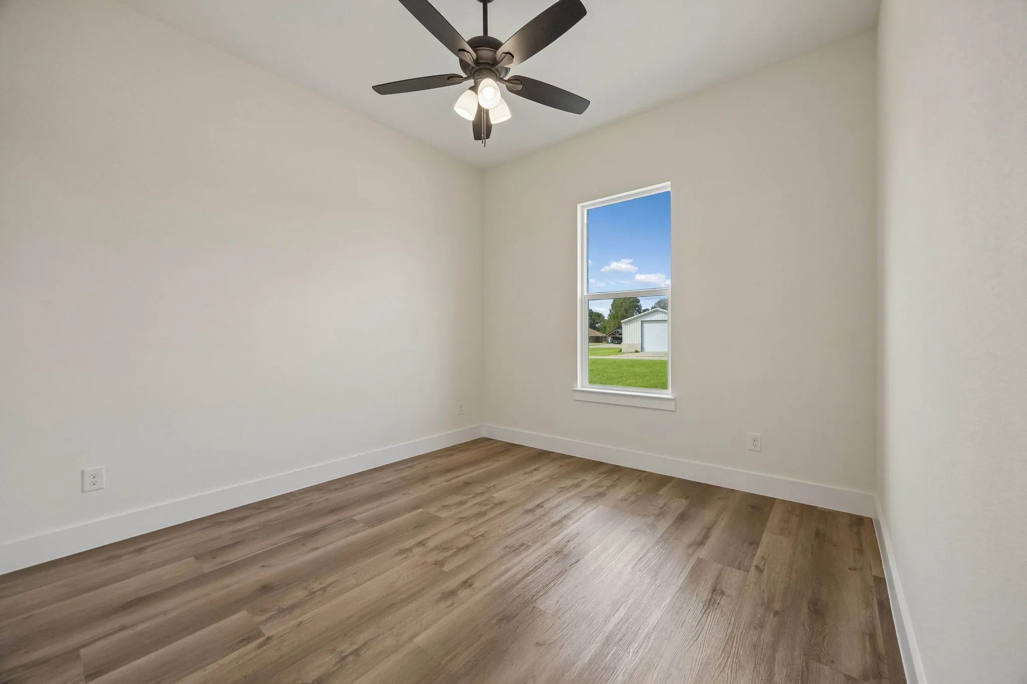 Wood-finish flooring, white trim, single window, and a ceiling fan with integrated lighting