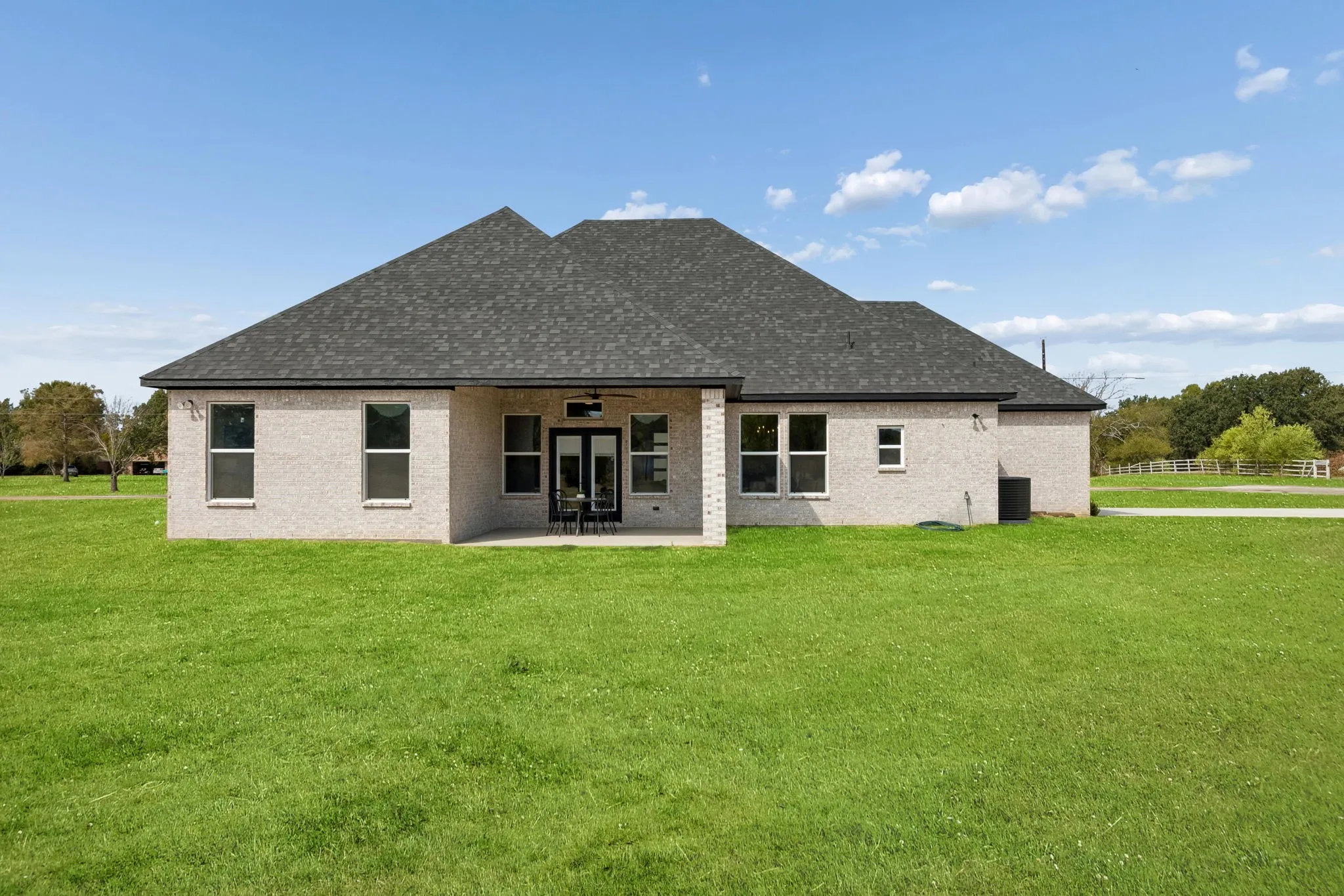Expansive rear yard featuring a covered patio, double glass-paneled doors, and multiple windows