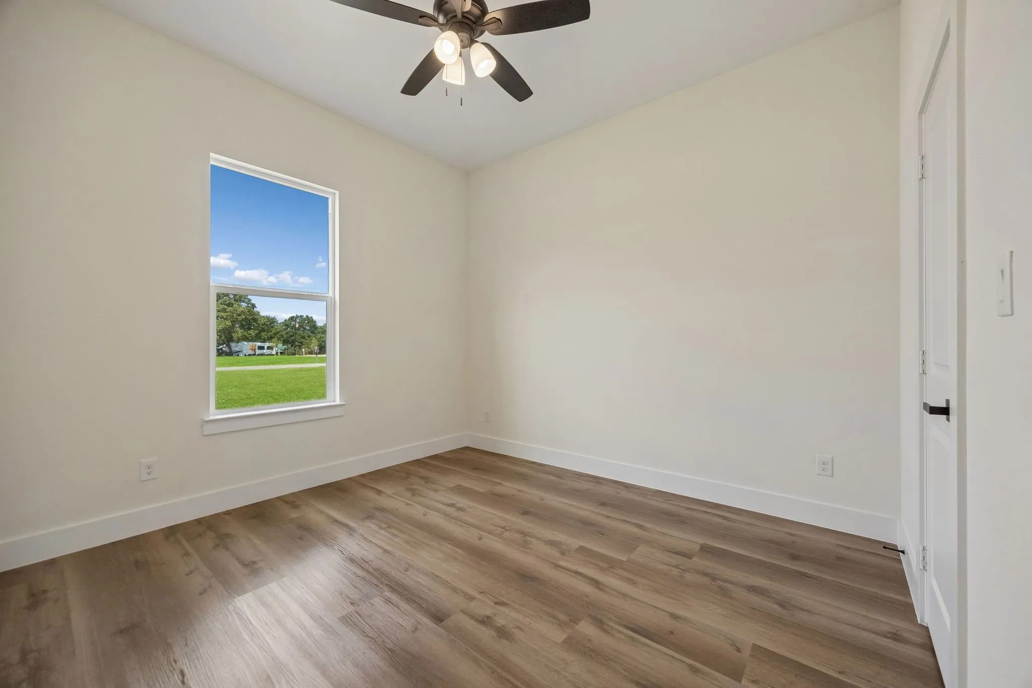 Neutral wall paint, wood-finish flooring, ceiling fan with integrated lighting, white trim, and a white door with black hardware