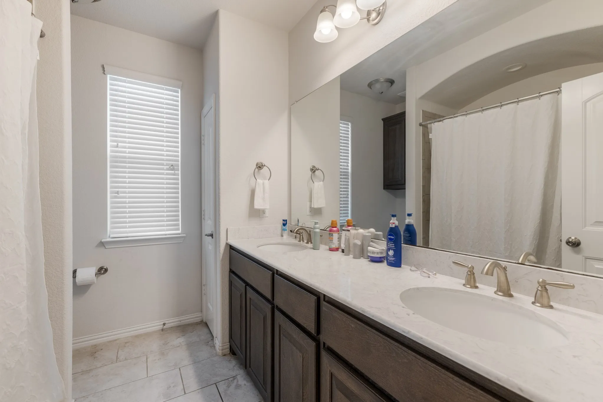 Dual vanity with brushed nickel fixtures, white countertop, dark wood-finish cabinetry, and tiled flooring