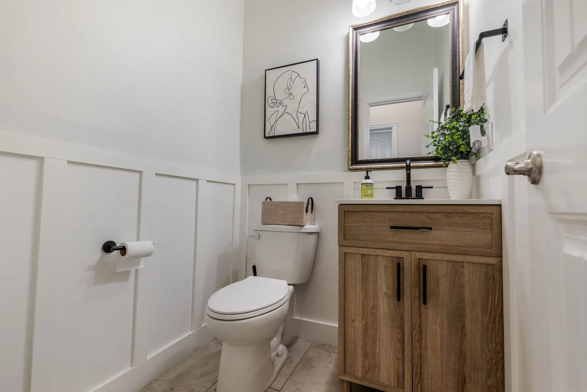 Spa-inspired bathroom featuring a wood-finish vanity with ample storage, black hardware accents, and a framed mirror with integrated lighting