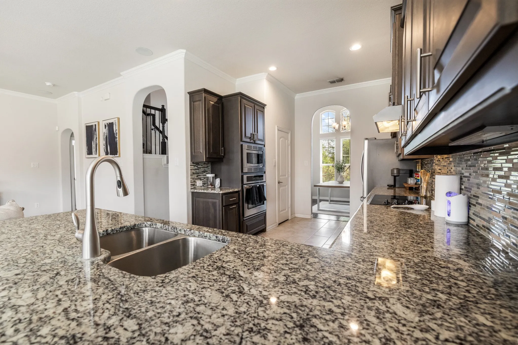 Kitchen featuring granite countertops, a double basin stainless steel sink, dark wood cabinetry, stainless steel appliances, and a tiled backsplash
