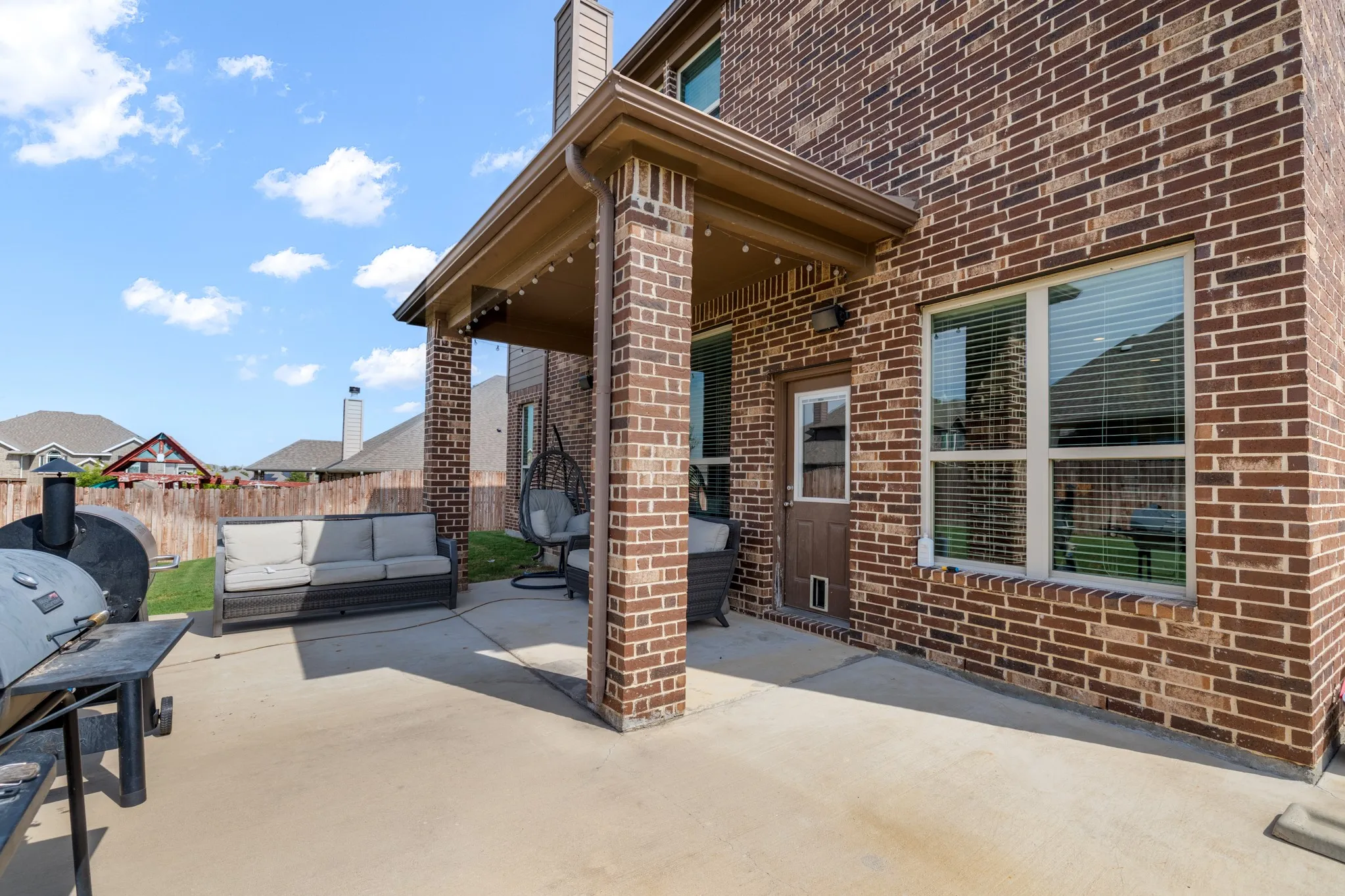 Covered patio featuring a concrete surface, brick columns, string lighting, and an exterior door with a pet access panel