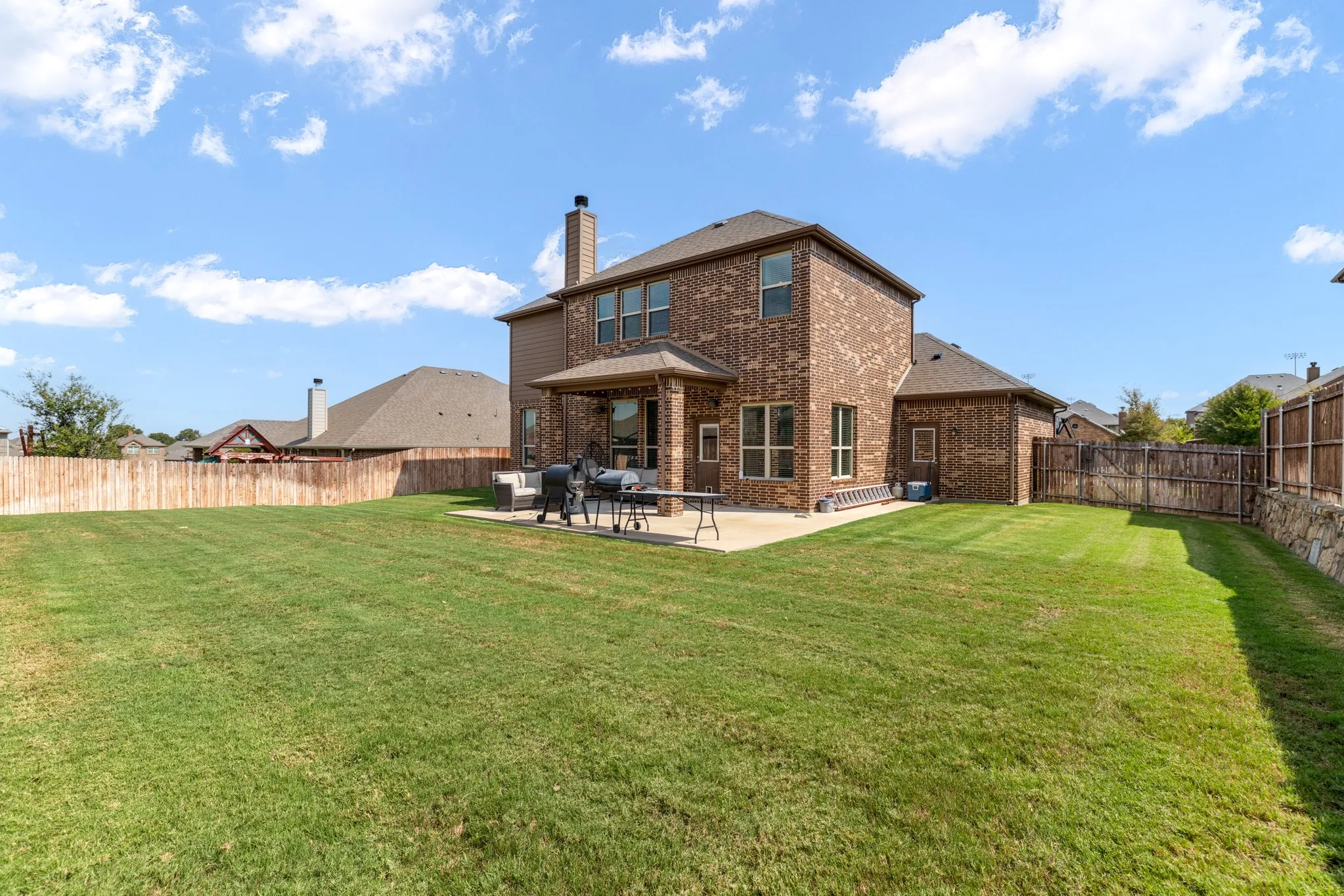 Expansive backyard featuring a manicured lawn, full brick exterior, a covered patio, and a privacy fence