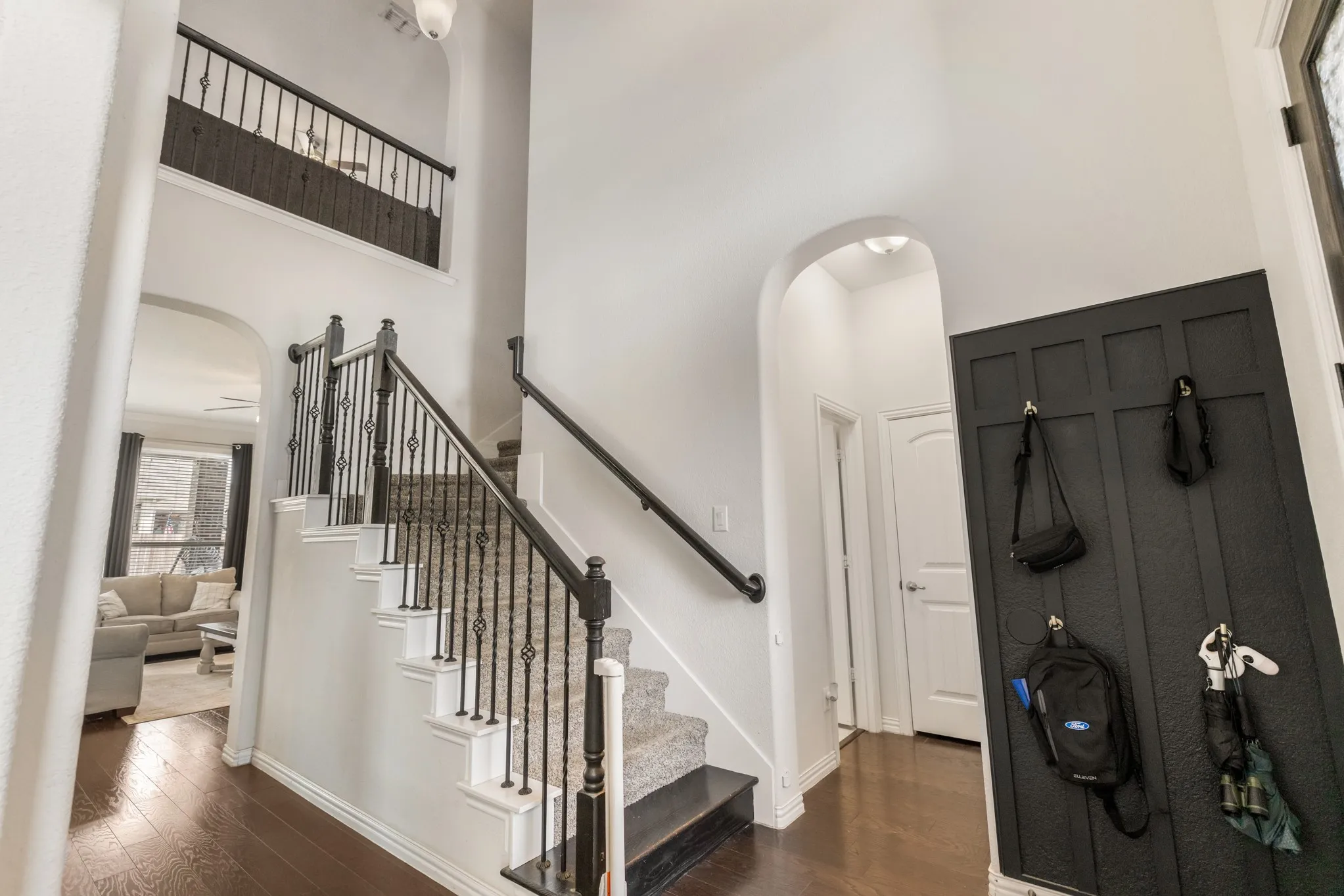 Foyer featuring wood-finish flooring, a carpeted staircase with ornate iron balusters, an arched doorway, and wainscoting