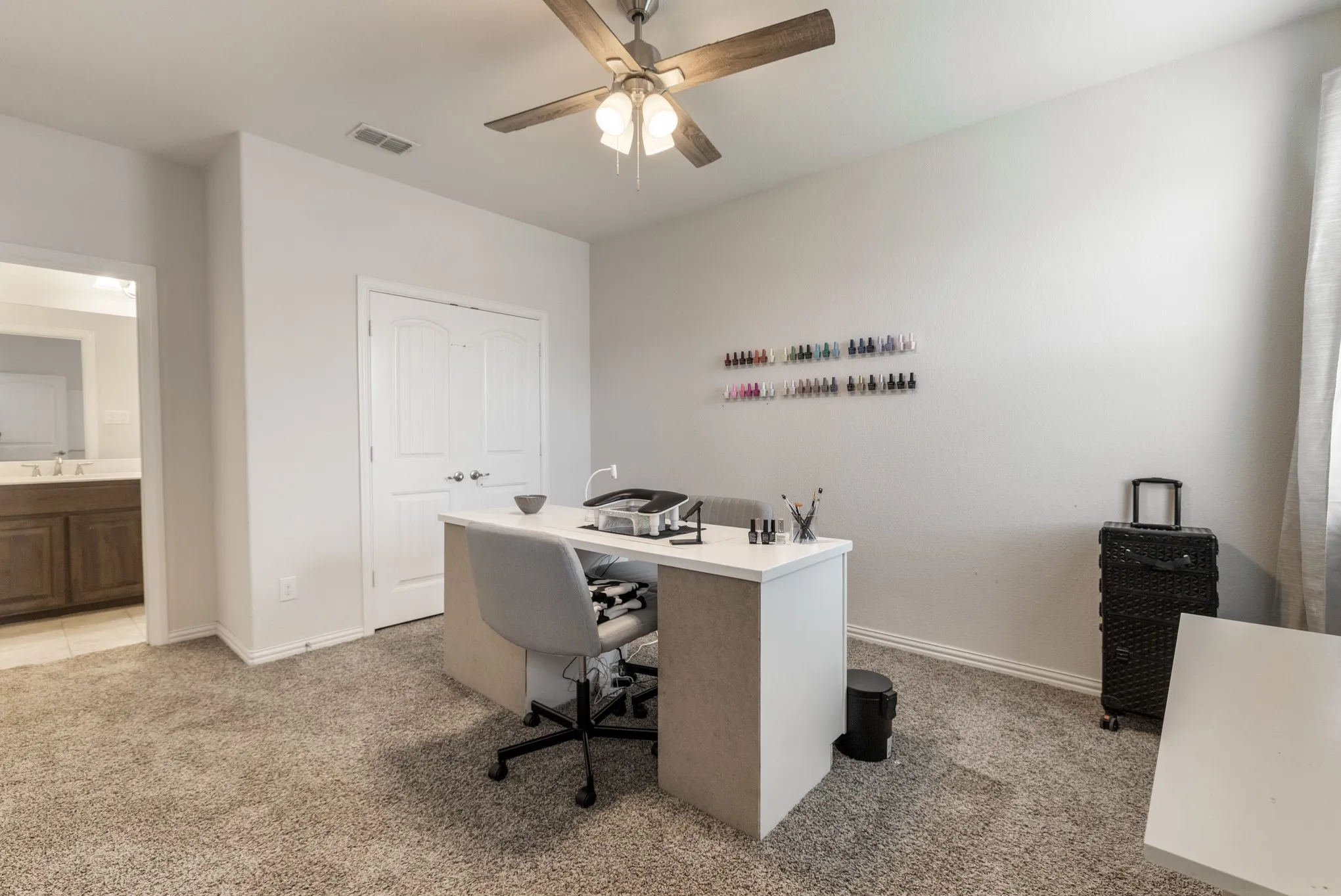Carpeted room with a ceiling fan, double doors, and a doorway opening to a vanity with wood-finish cabinetry