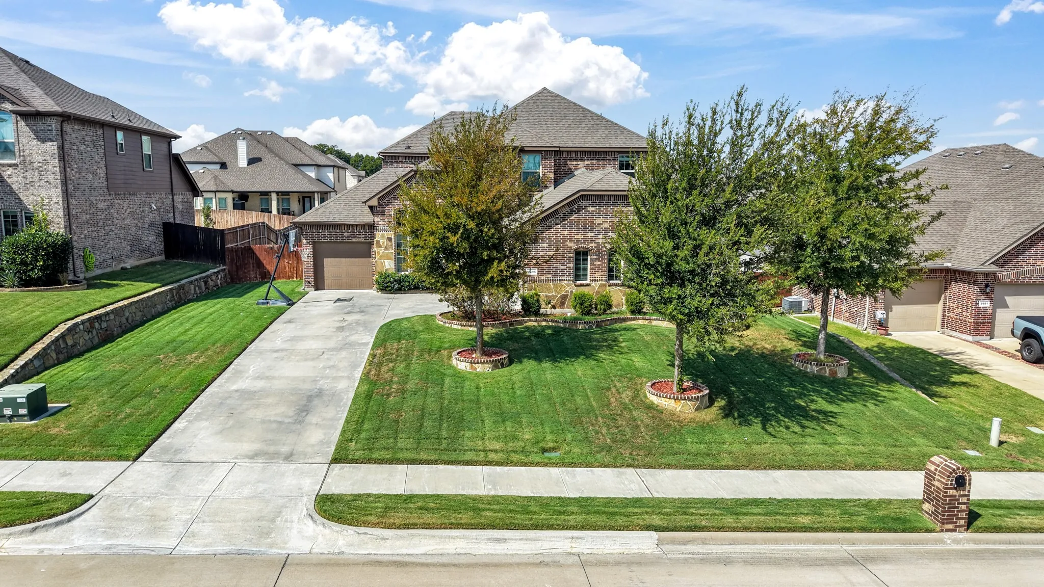Brick exterior residence with a two-car garage, concrete driveway, and mature landscaping
