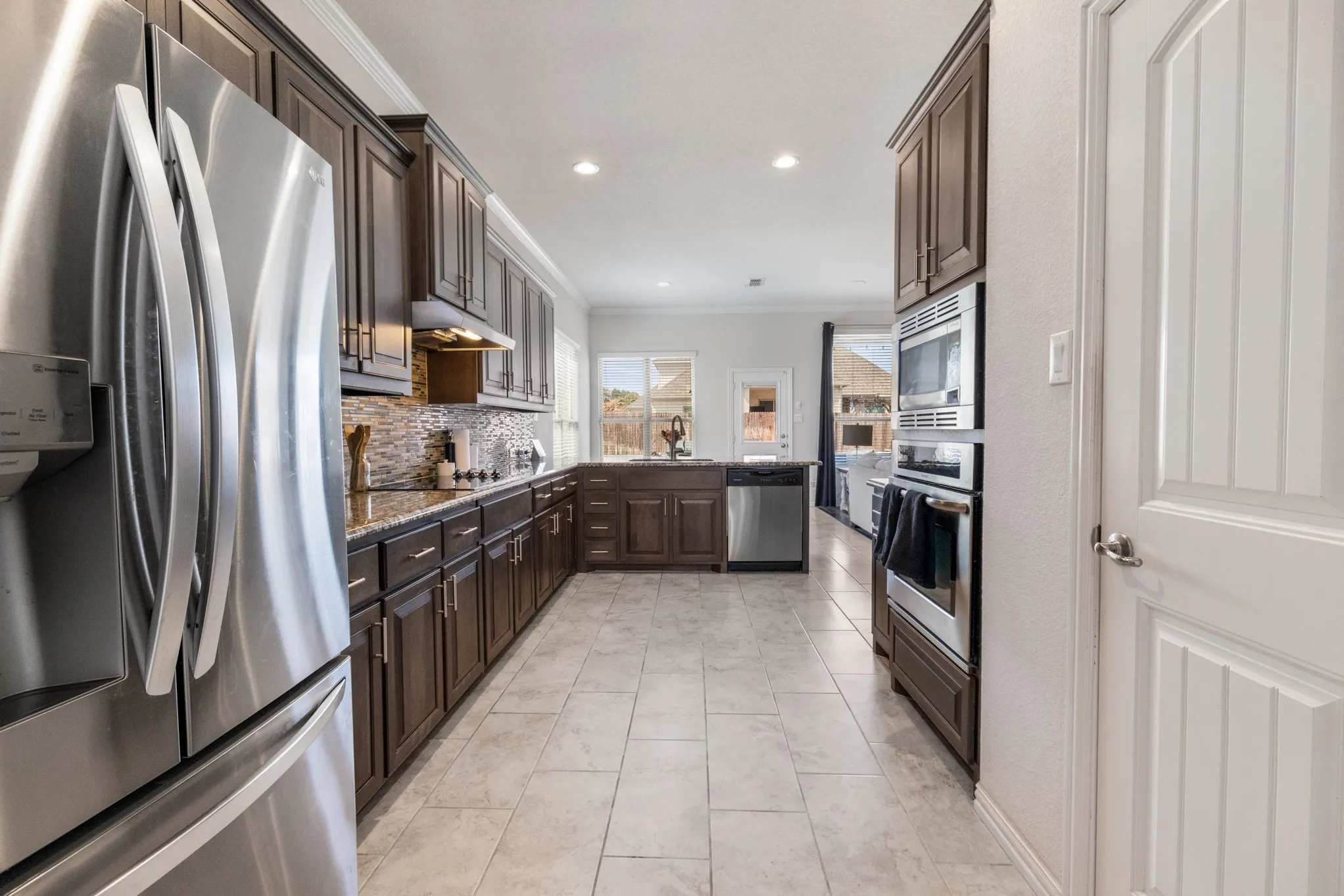 Stainless steel appliances, built-in oven and microwave, dark wood cabinetry, tile flooring, and granite countertops
