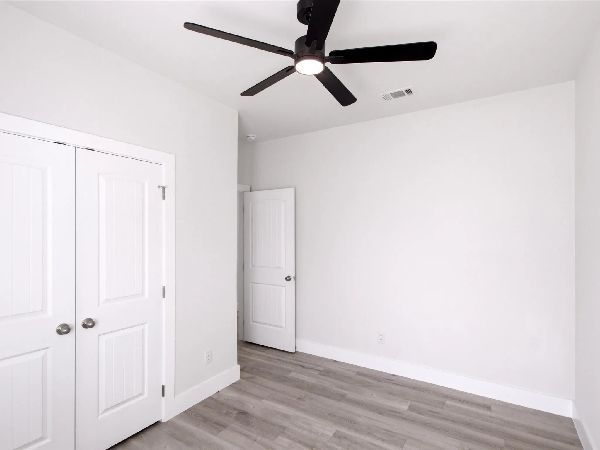 Bright interior with wood-finish flooring, white paneled doors, and a ceiling fan with integrated lighting
