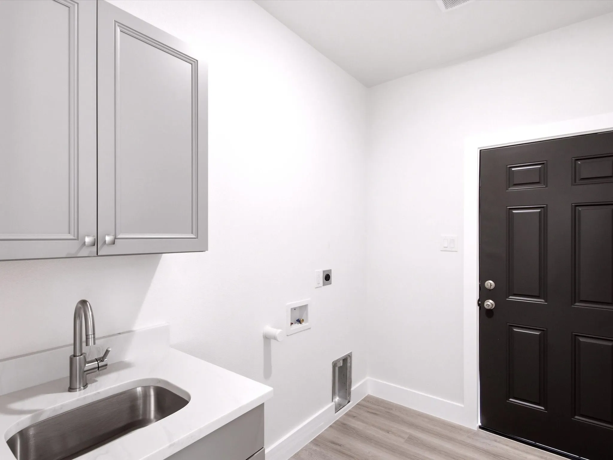 Light gray shaker cabinetry, stainless steel sink, white countertop, wood-finish flooring, and a paneled dark door