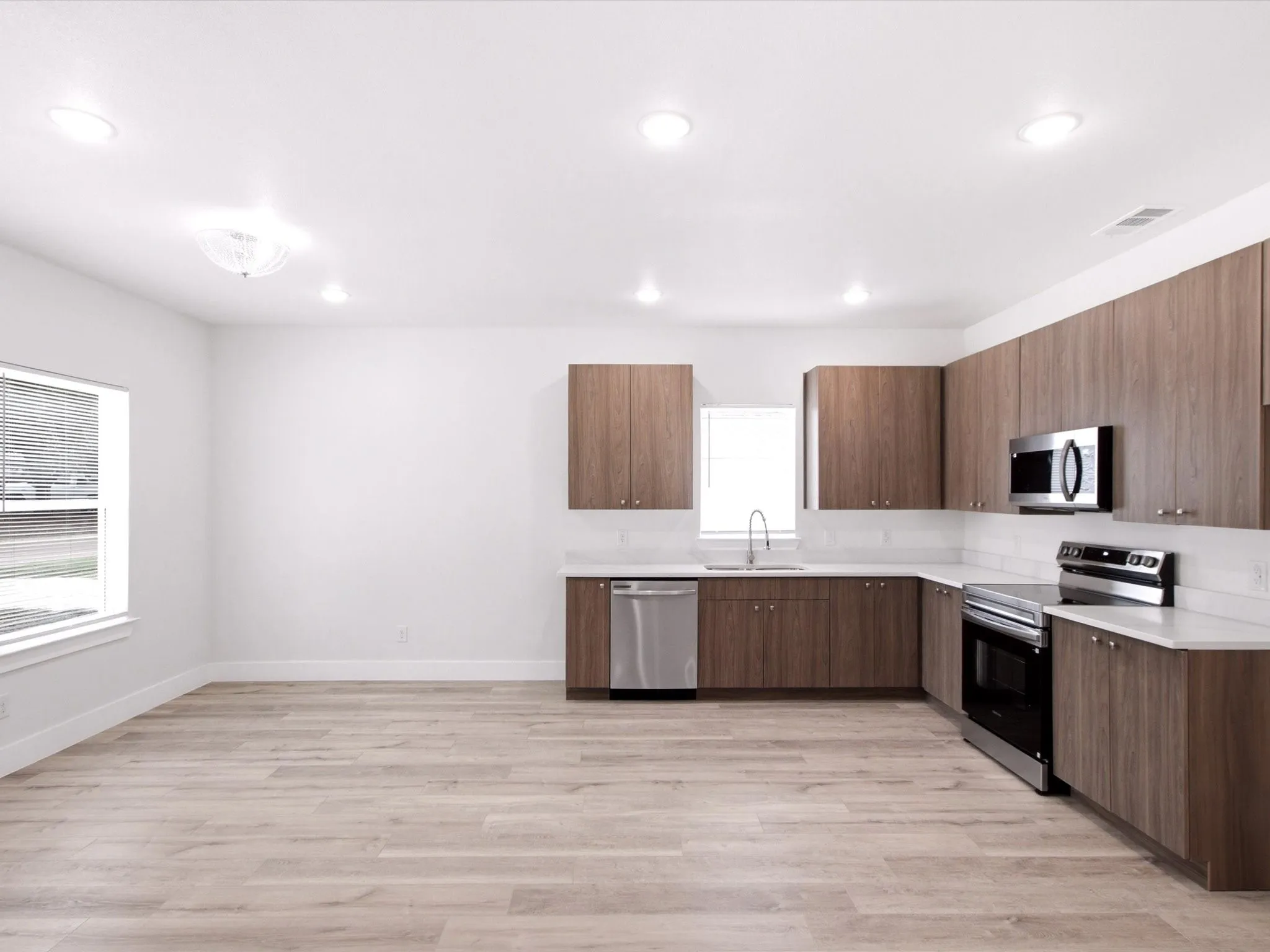 Open-concept kitchen with wood-finish cabinetry, stainless steel appliances, white subway tile backsplash, and light wood-finish flooring