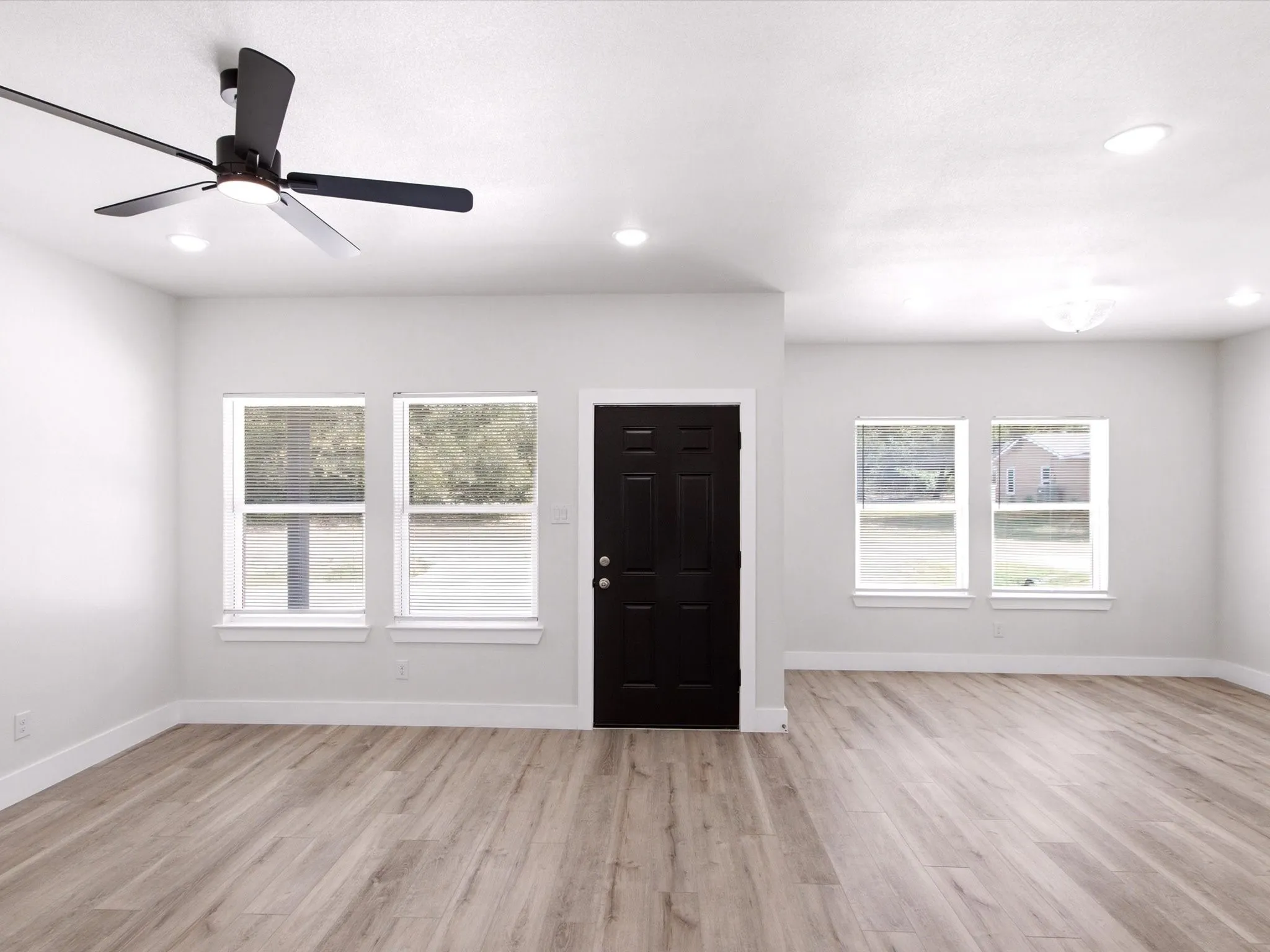 Bright, open living space featuring wood-finish flooring throughout, recessed ceiling lighting, and a ceiling fan with integrated lighting