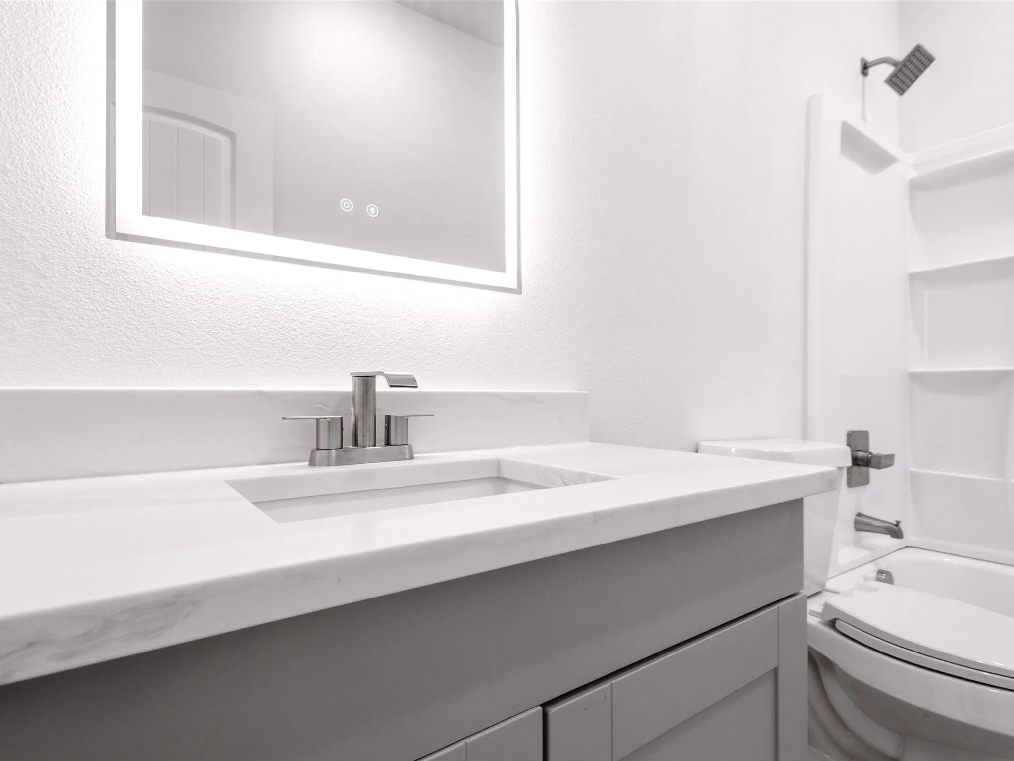Vanity with a light gray finish, solid surface countertop, integrated sink, and an illuminated mirror