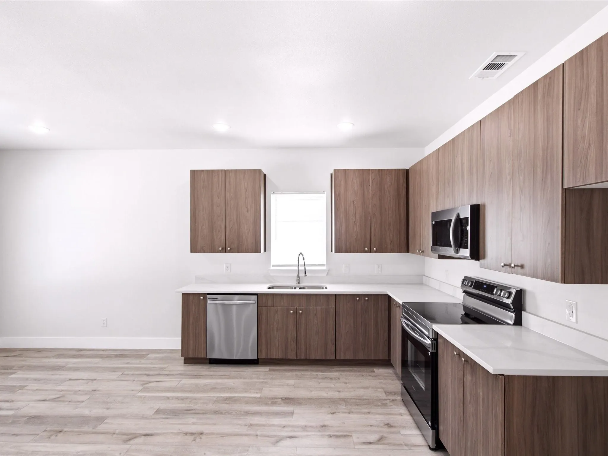 Wood-finish flooring, white countertops, built-in stainless steel appliances, and dark wood-finish cabinetry