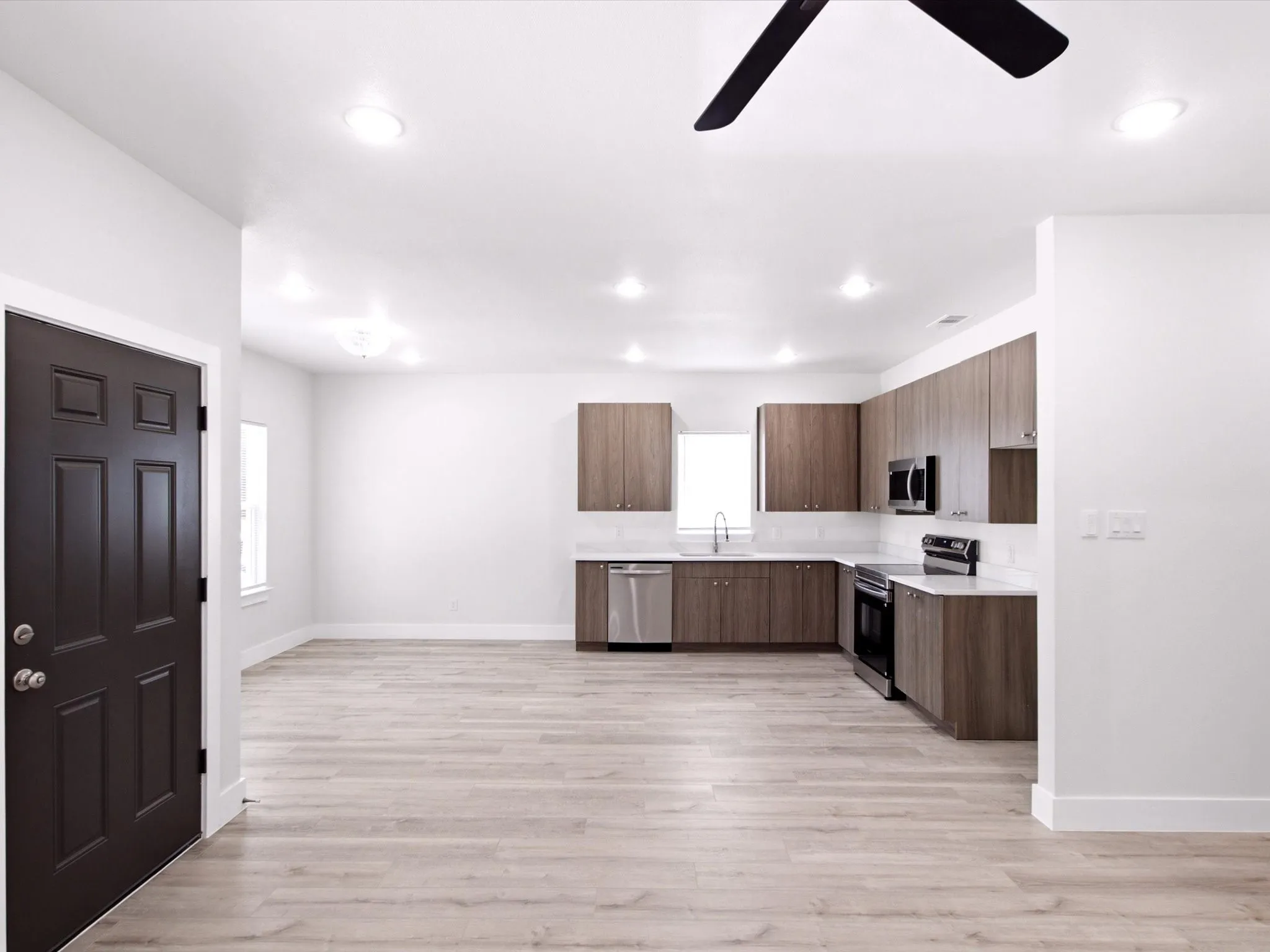 Open-concept living space with wood-finish flooring, recessed lighting, and a modern kitchen featuring wood-finish cabinetry, stainless steel appliances, and white countertops