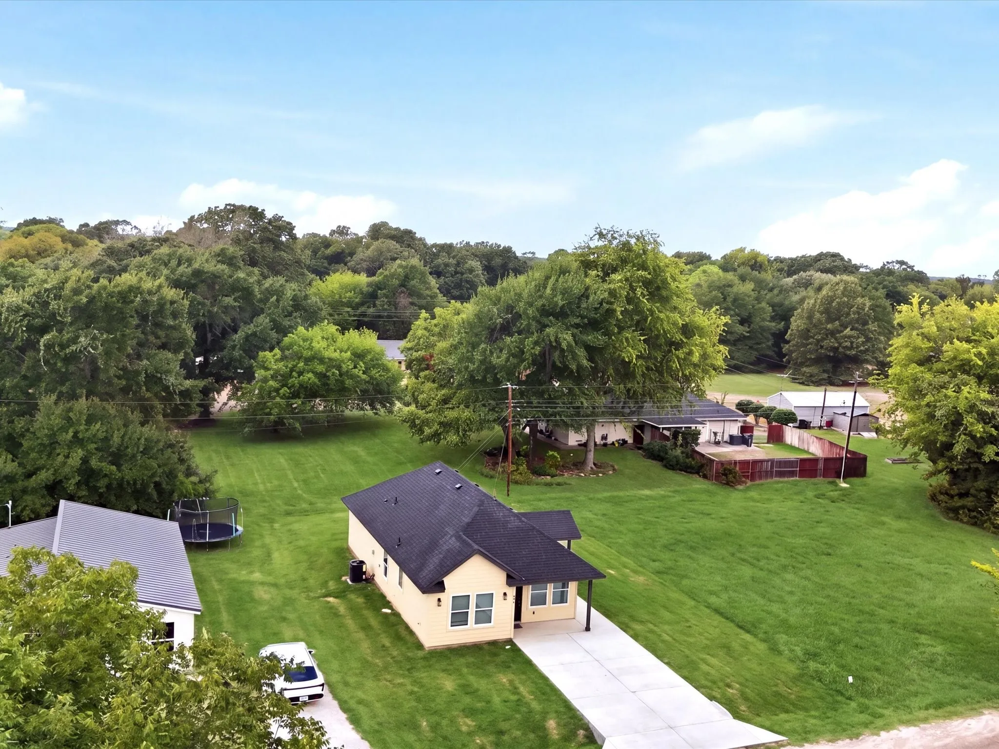 Light-colored exterior with a dark shingle roof, expansive green lawn, and mature trees