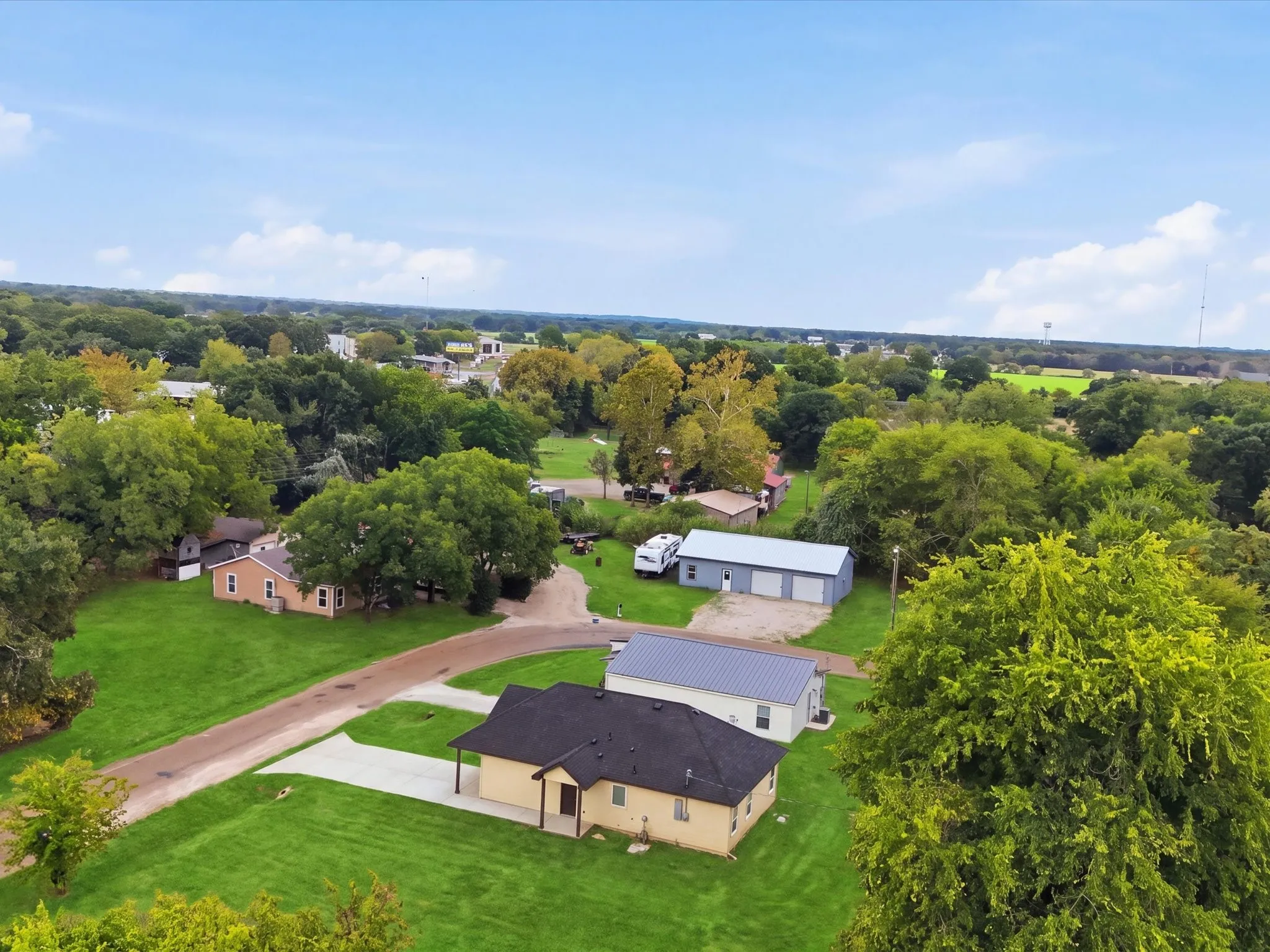 Expansive property with a single-story residence featuring a dark shingle roof and a cream-colored exterior, accompanied by a separate multi-bay garage structure