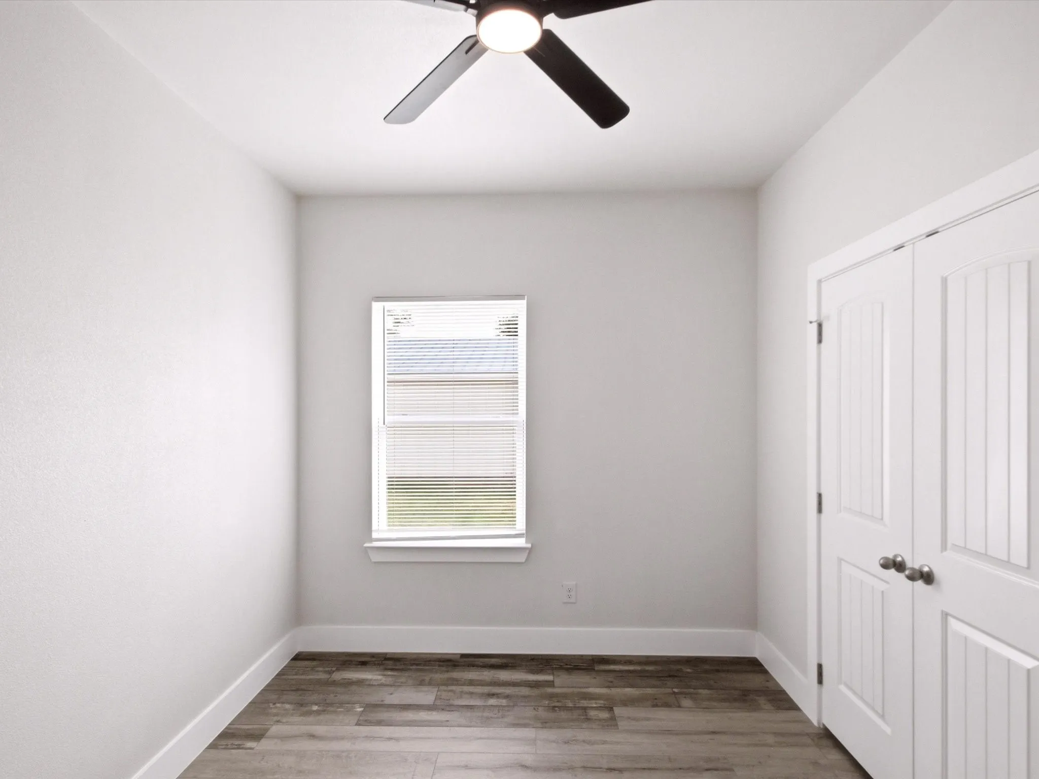 Wood-finish flooring, white walls, and a window with blinds