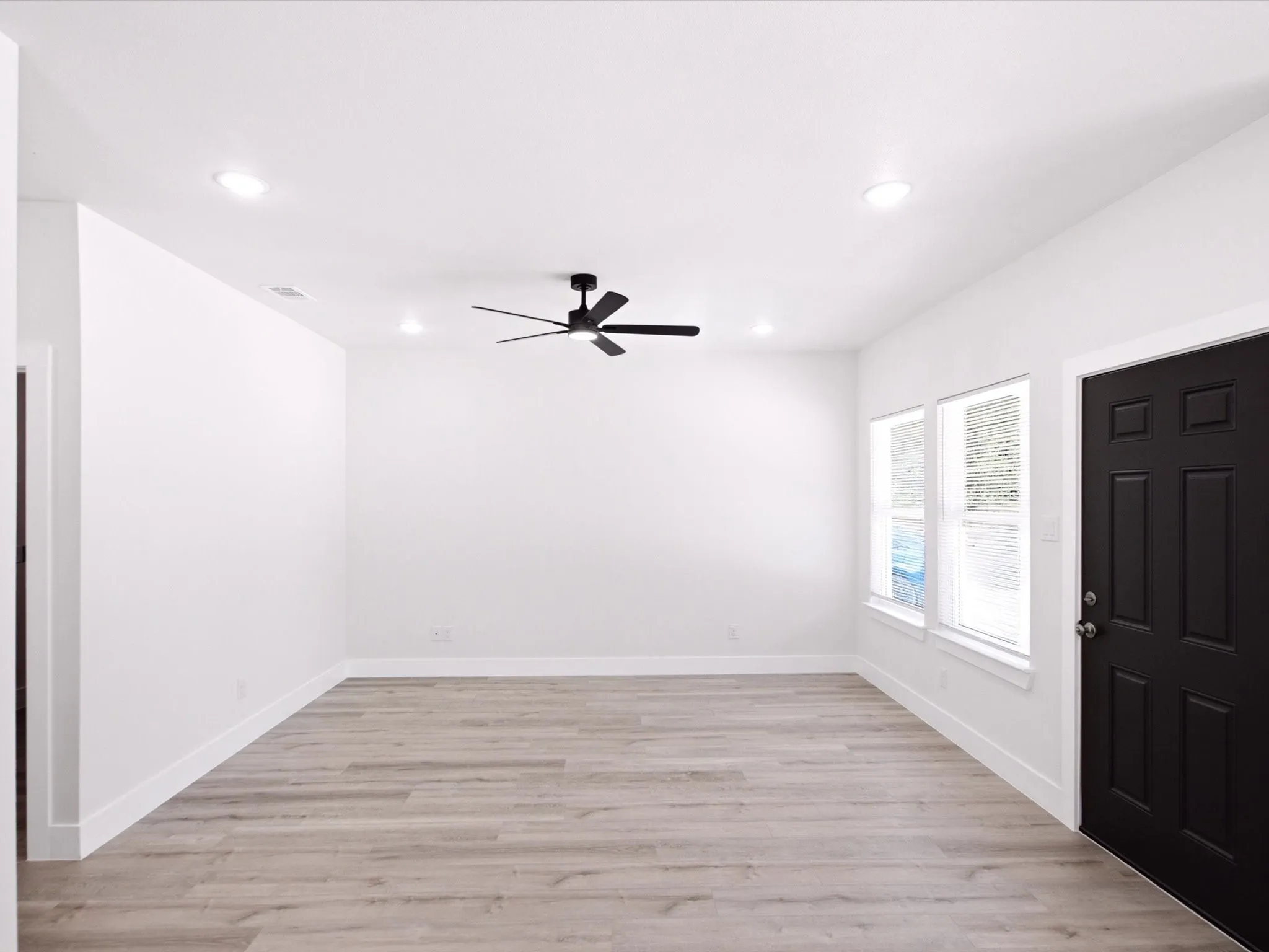 Recessed ceiling lighting, wood-finish flooring, white walls, and a black ceiling fan