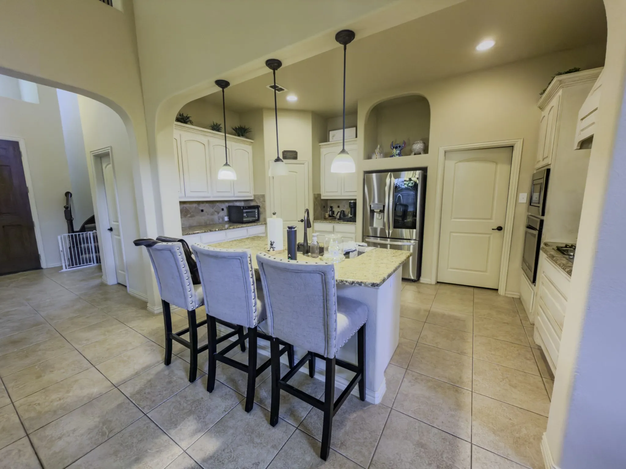 Kitchen featuring an expansive island with a light-toned countertop, white cabinetry, integrated stainless steel refrigerator, and tiled flooring