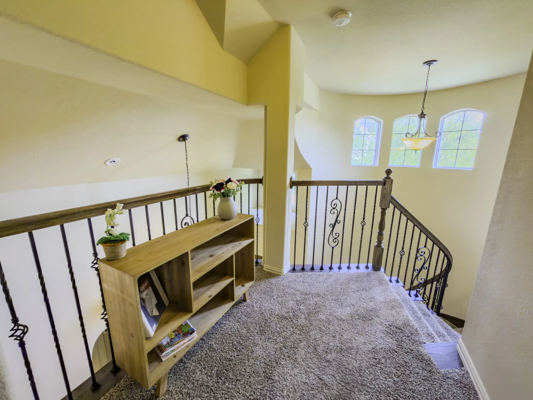 Loft area with carpet flooring, wrought iron railing, arched windows, and a hanging light fixture