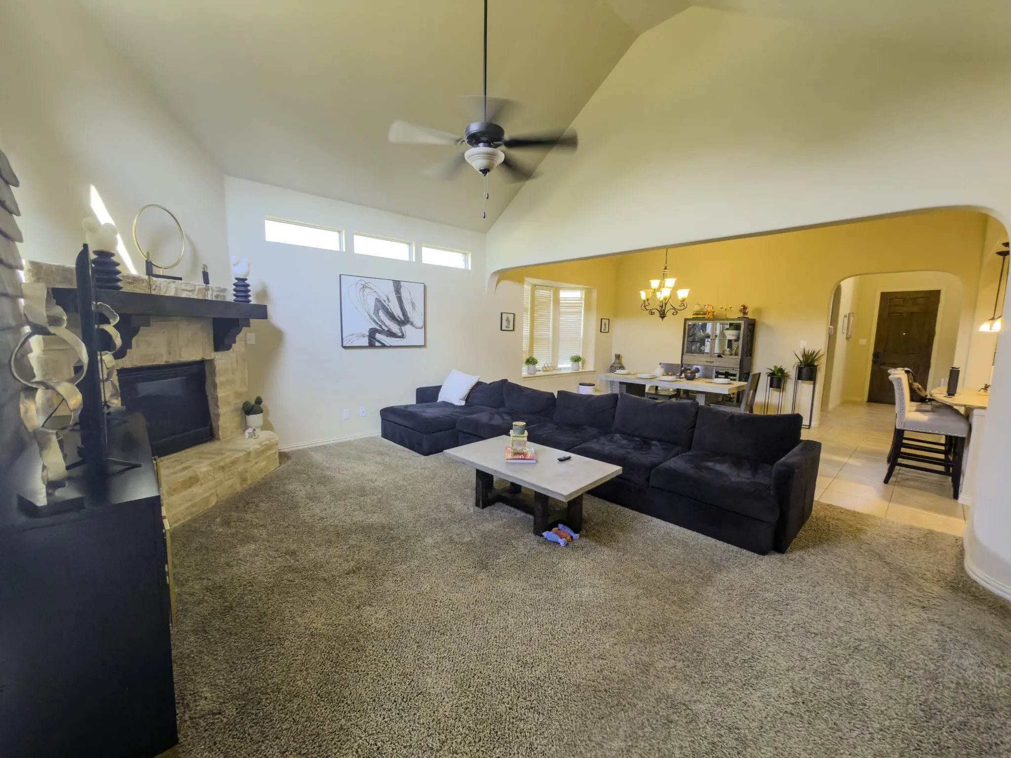 Spacious living area featuring a vaulted ceiling and stone-faced fireplace with a wood mantel