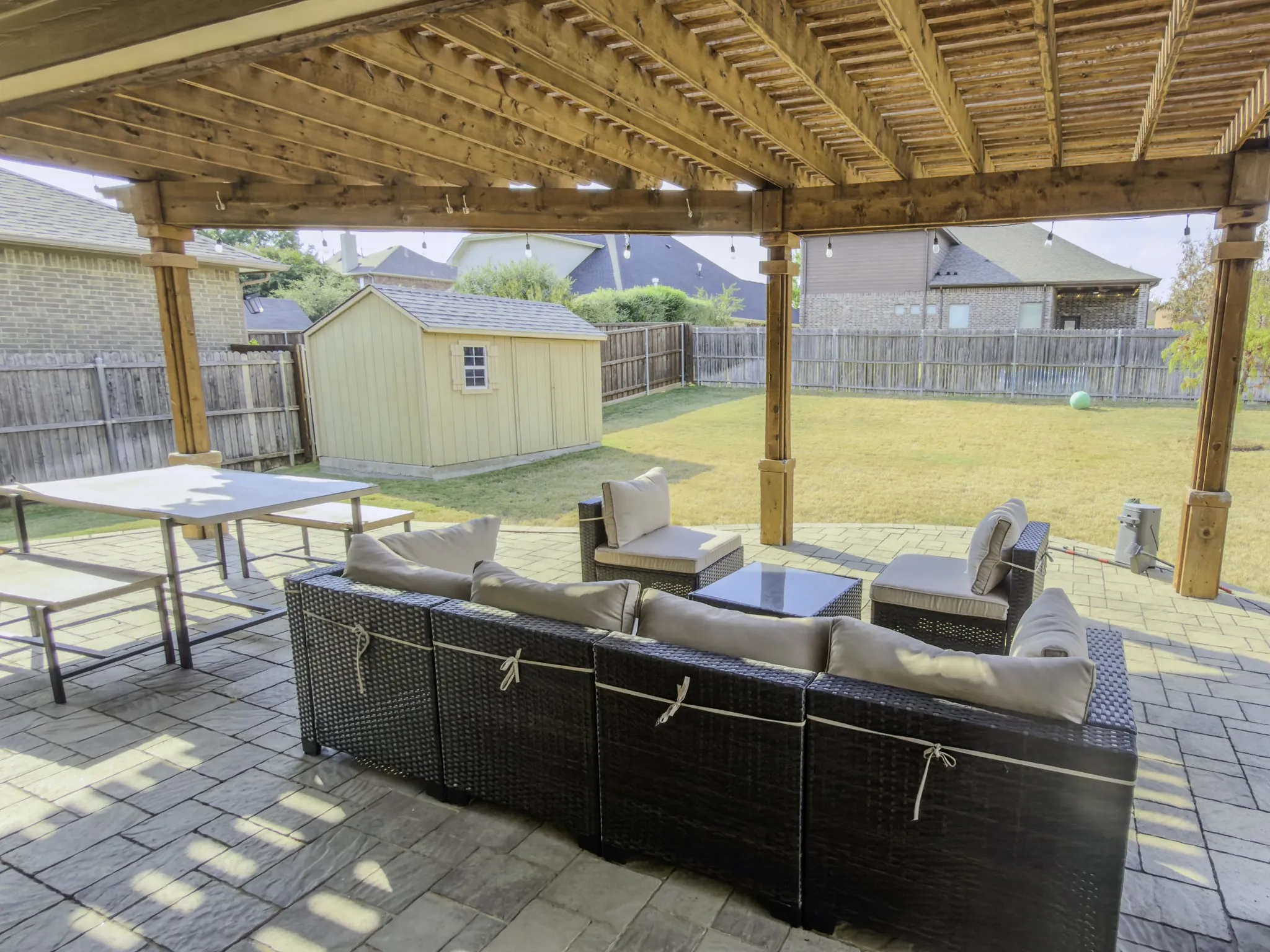 Expansive paver patio with a wood pergola, featuring a large grassy yard and a detached shed structure