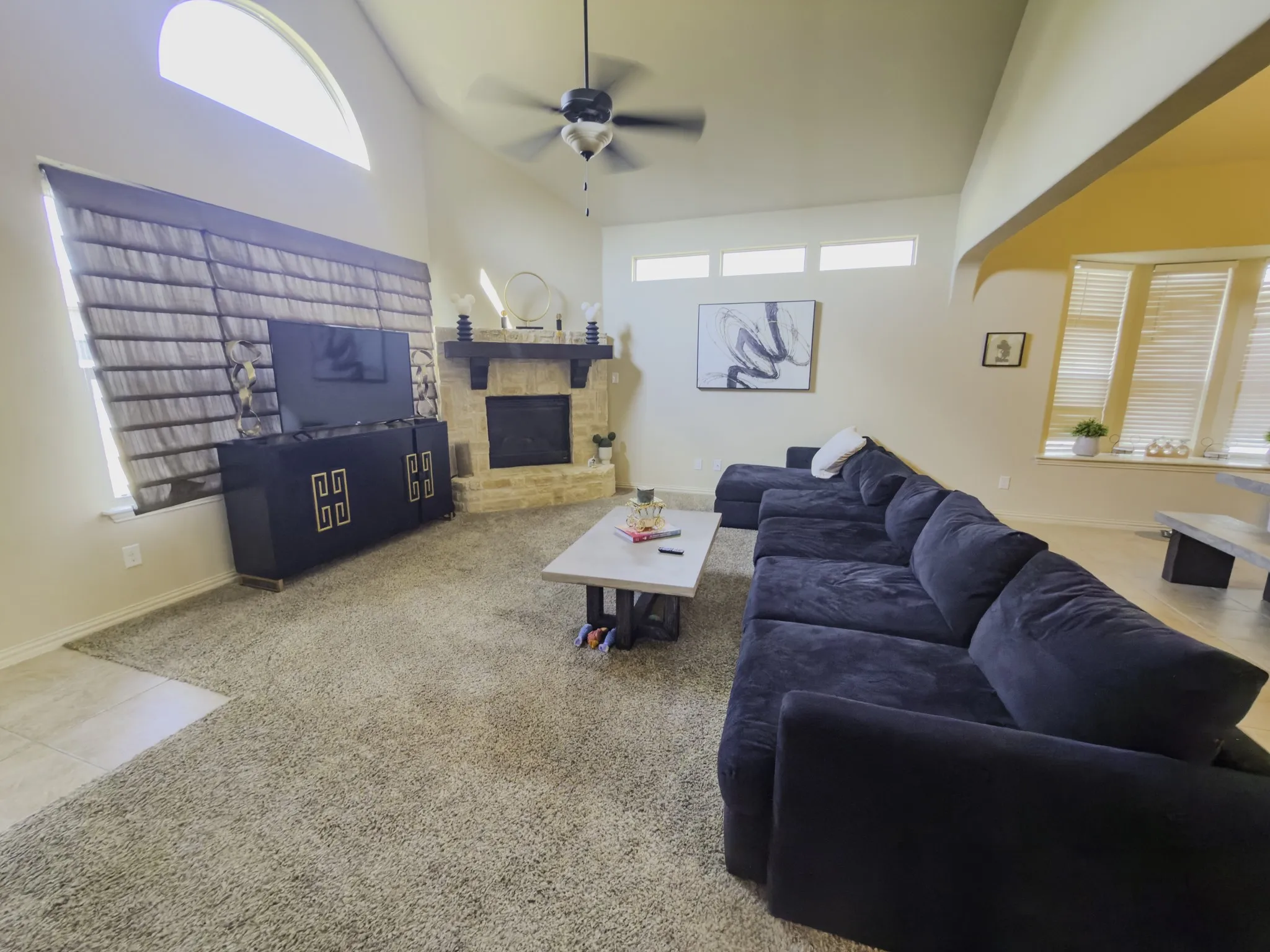 Vaulted ceilings with a ceiling fan, stone-clad fireplace, arched window, and carpet flooring