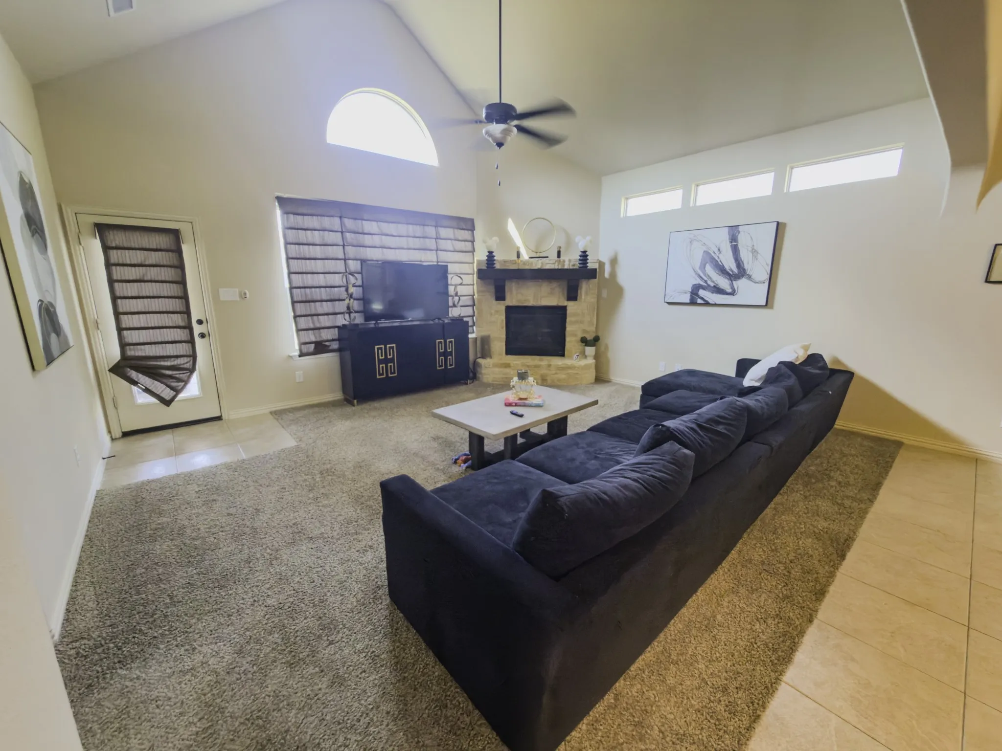 Vaulted ceiling, stone fireplace with mantel, ceiling fan, transom windows, and tile flooring