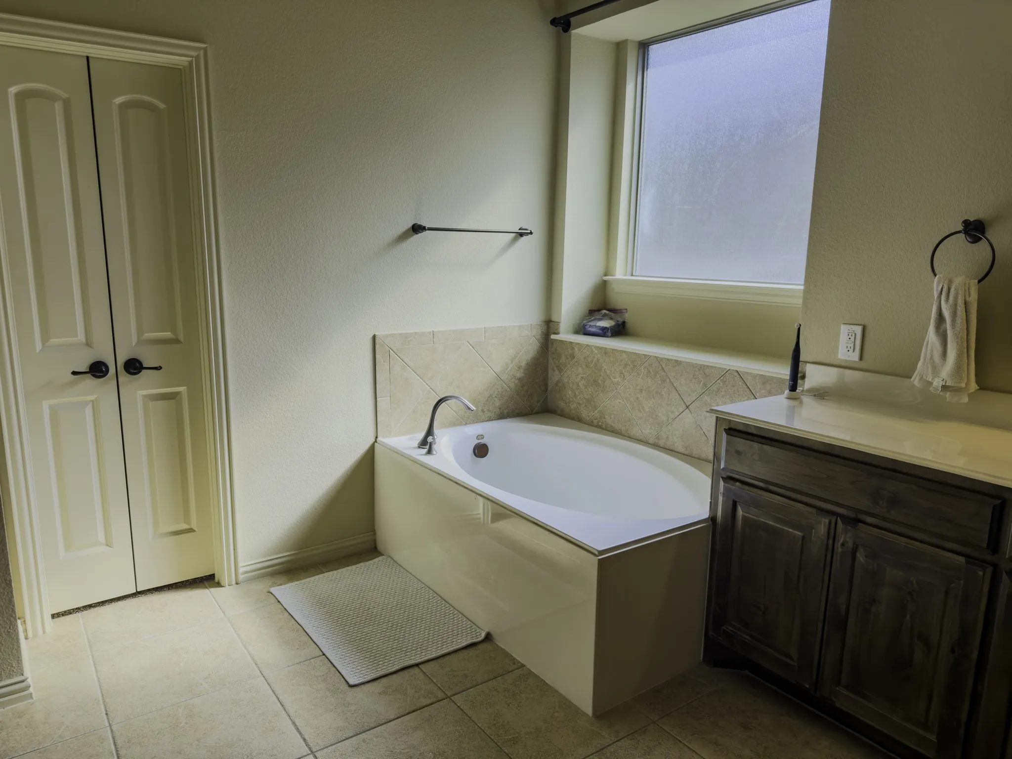Built-in soaking tub with tile surround, wood-finish vanity with countertop, and double-panel doors