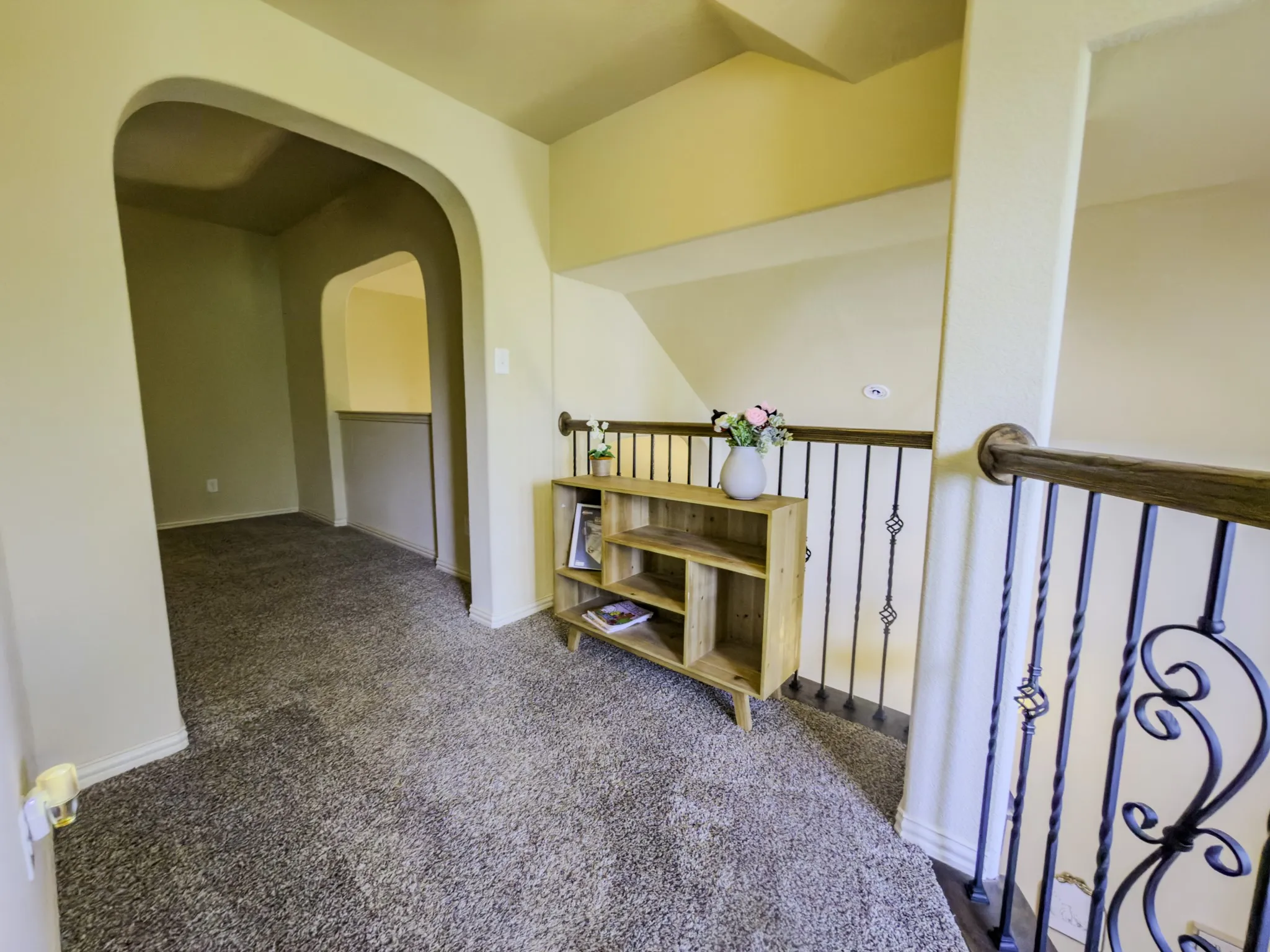 Arched entryway, carpeted flooring, black wrought iron railing, and wooden handrail