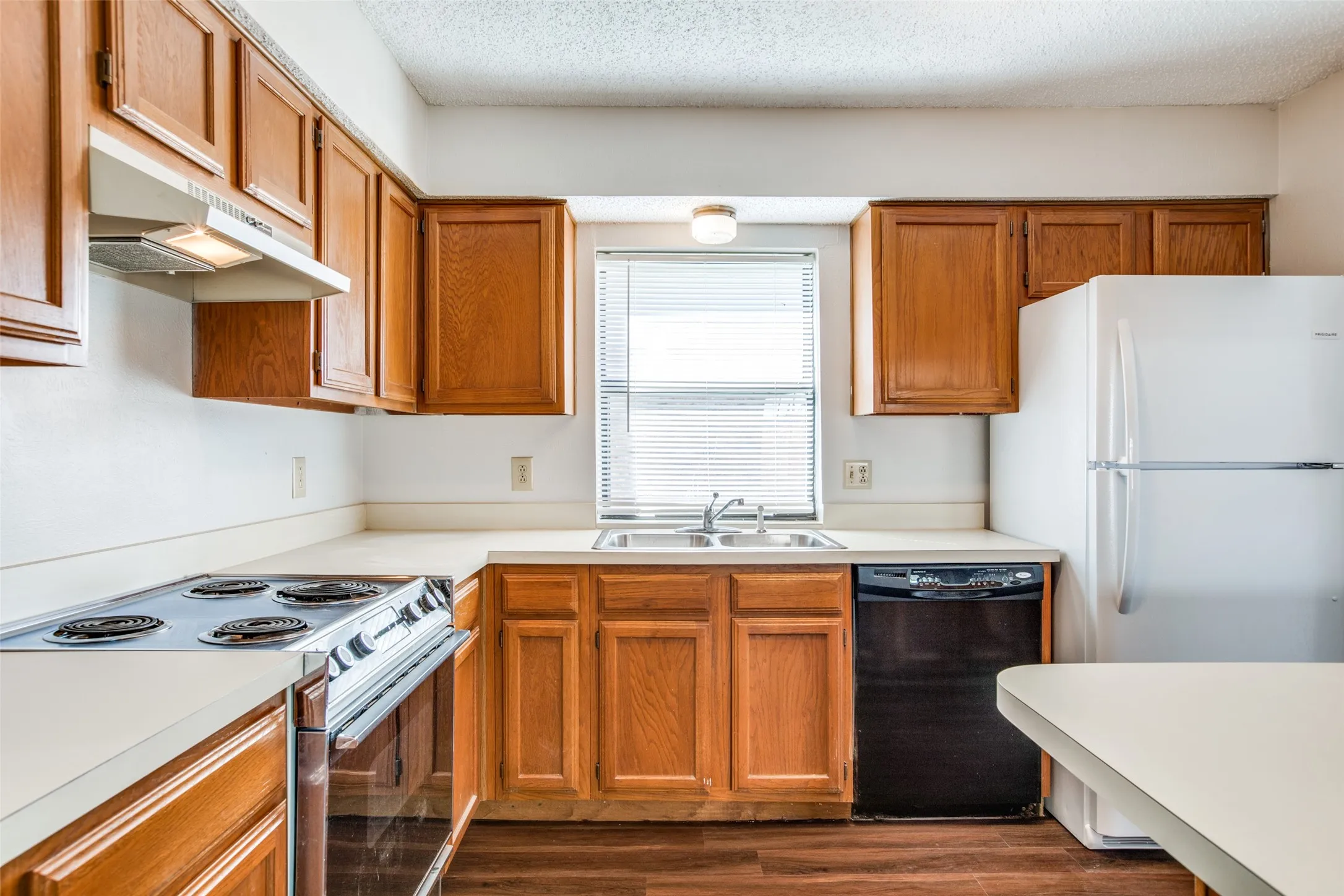 Kitchen featuring wood cabinetry, light-toned countertops, stainless steel sink, black dishwasher, and a white refrigerator