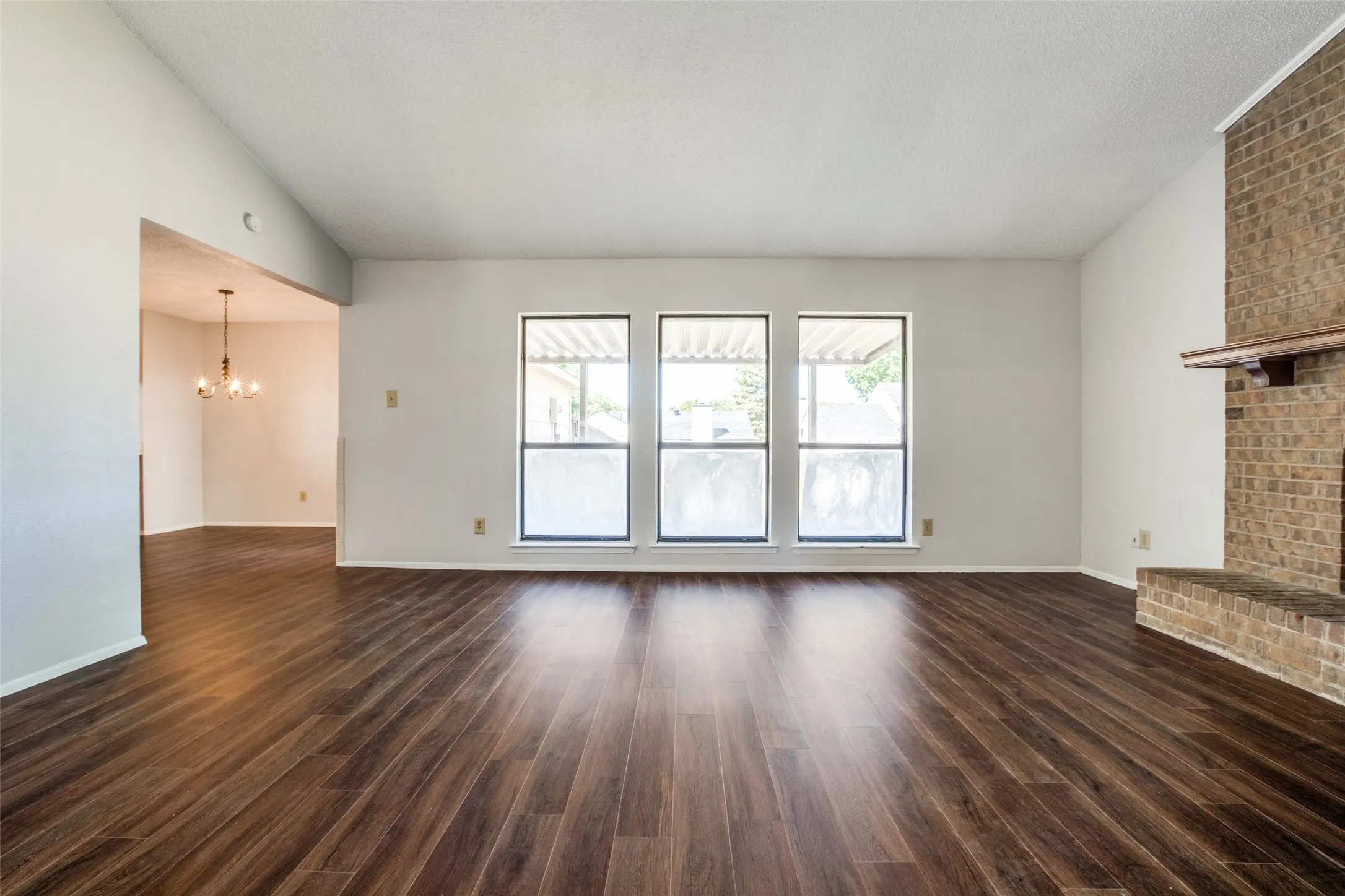 Spacious living area featuring wood-finish flooring, a brick fireplace with a wood mantle, and three large windows